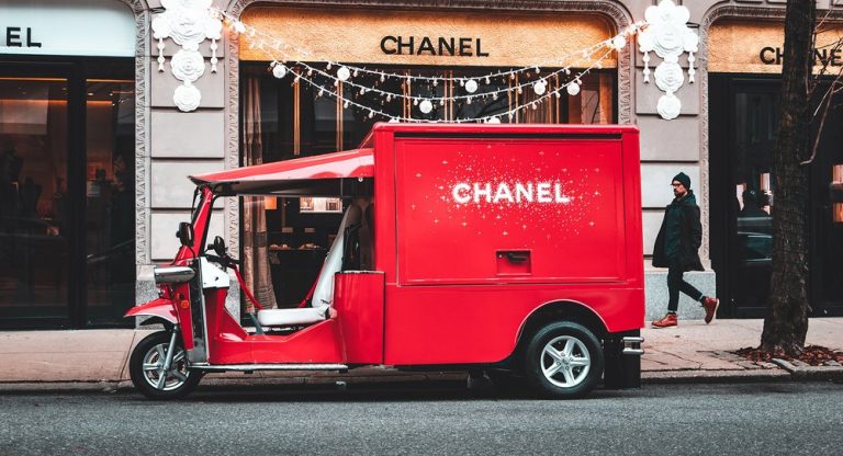 Red Chanel tuk-tuk parked outside a Chanel store with festive lights; person walking by.