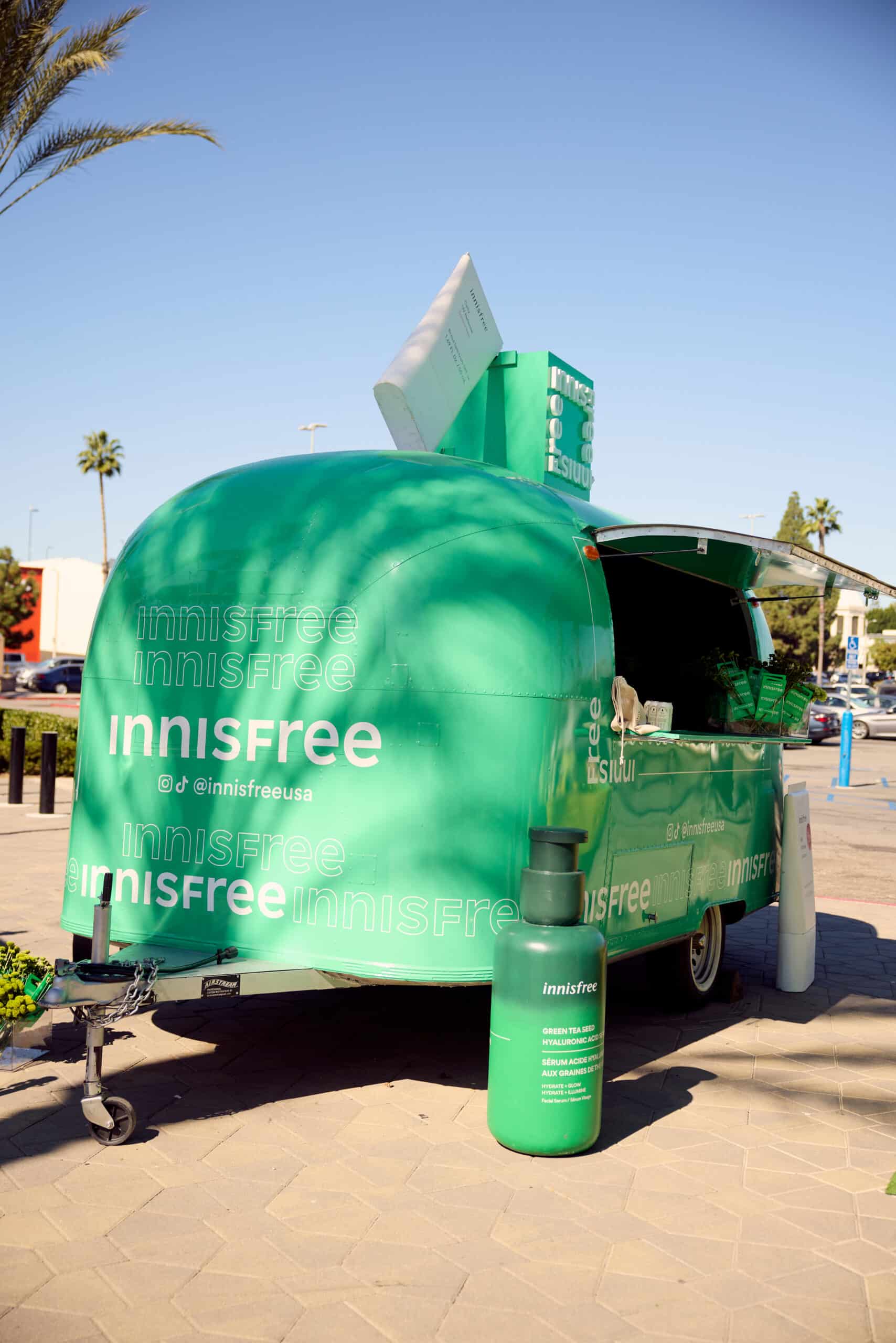 Green Innisfree trailer with branding parked outdoors beside a large product replica bottle.