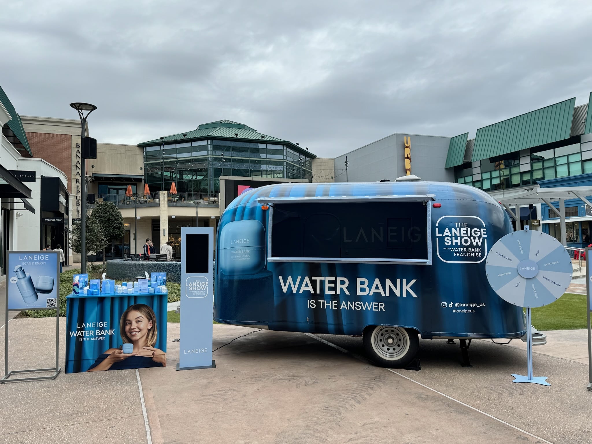 Blue Laneige Water Bank trailer outdoors with promo displays, prize wheel, samples, and signage.