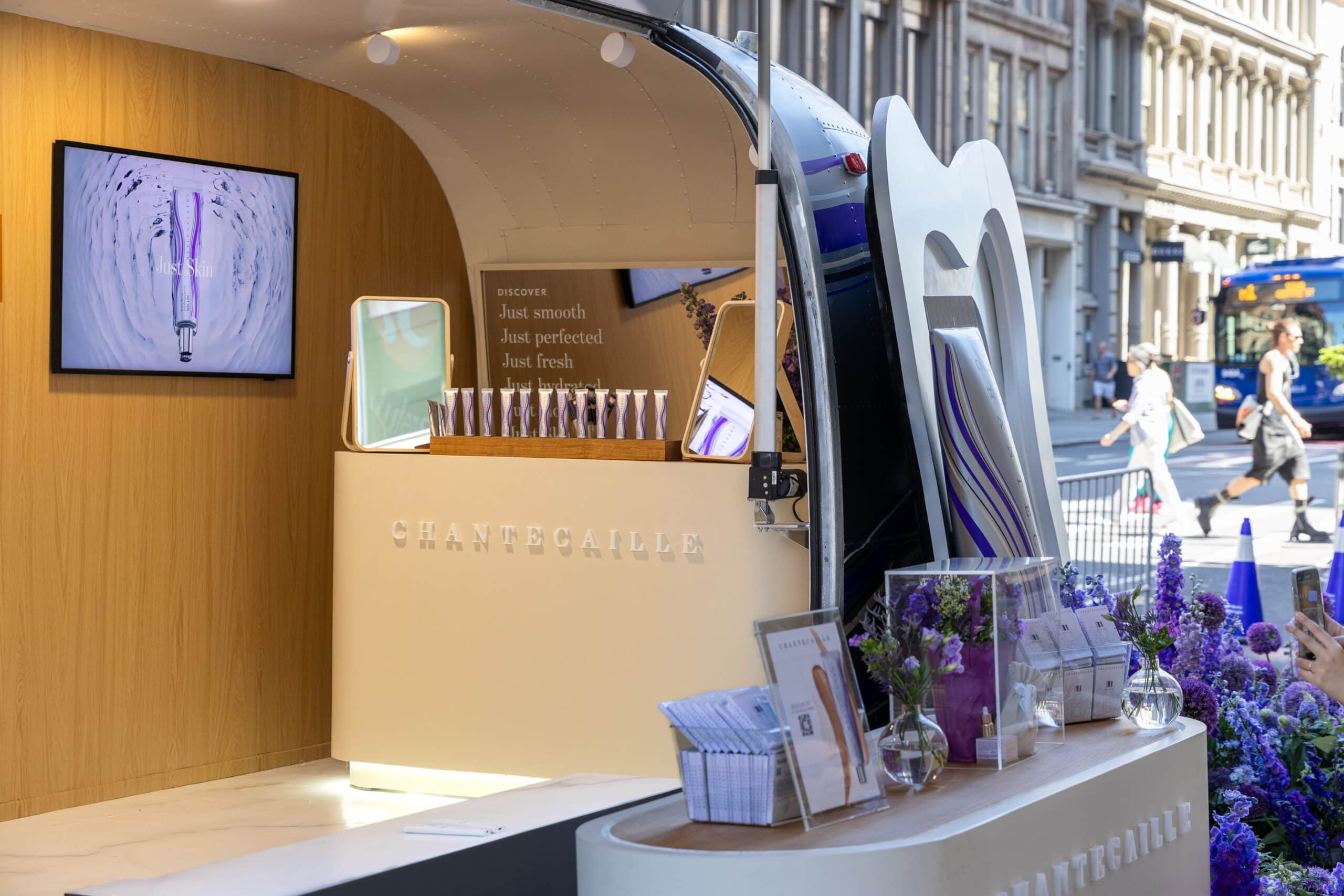 Chantecaille pop-up in an airstream trailer displays skincare, signs, and flowers on a city street.