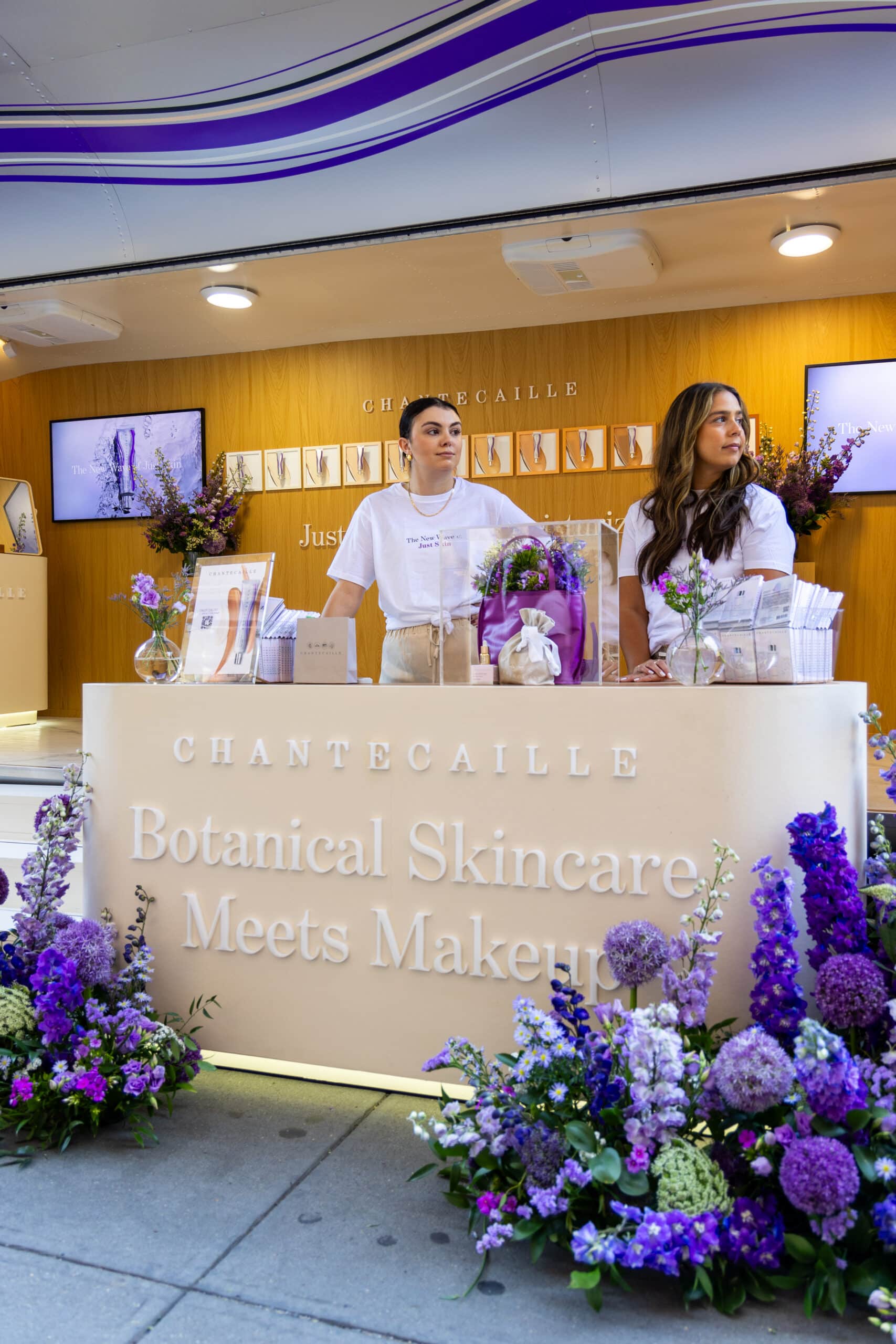 Two people at a Chantecaille booth by an Airstream trailer with flowers and skincare products.