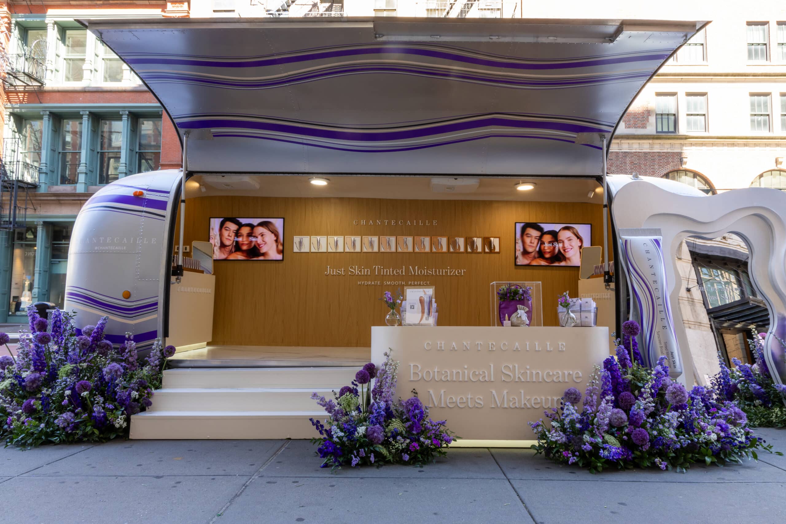 Airstream pop-up with purple and white flowers promotes tinted moisturizer and diverse models.