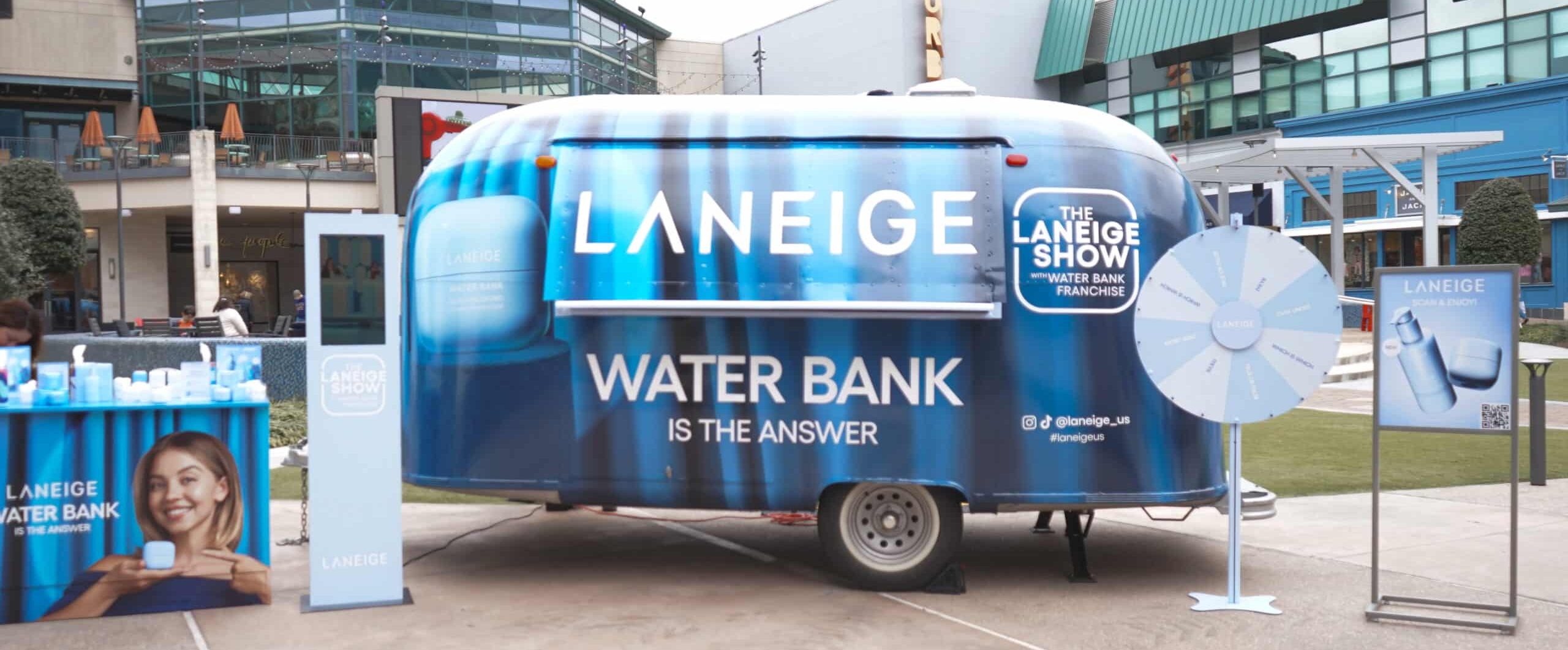 Blue Laneige trailer outdoors with “WATER BANK IS THE ANSWER”, skincare, and promo poster.