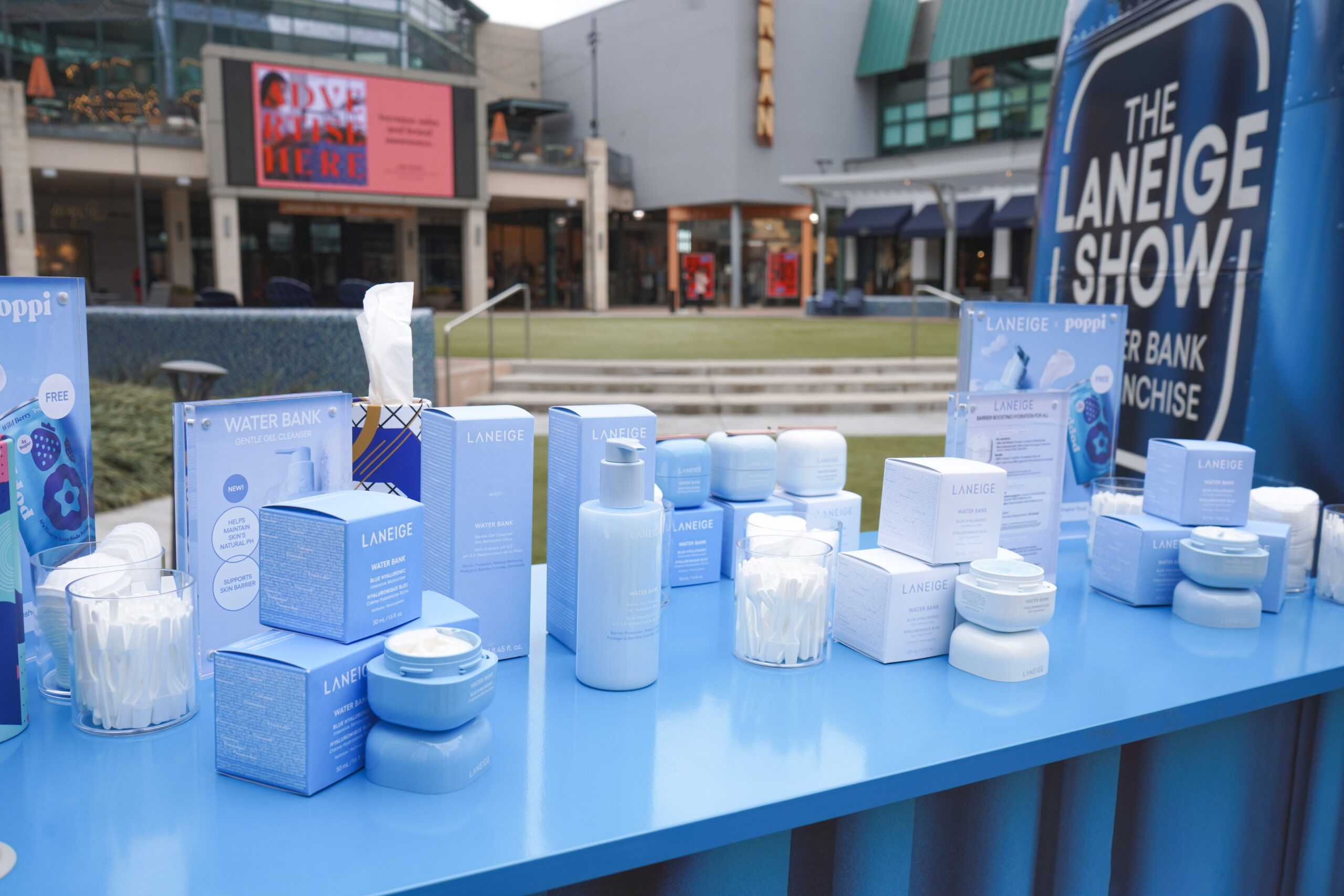 Laneige skincare products in blue and white packaging on an outdoor table with a promo sign nearby.