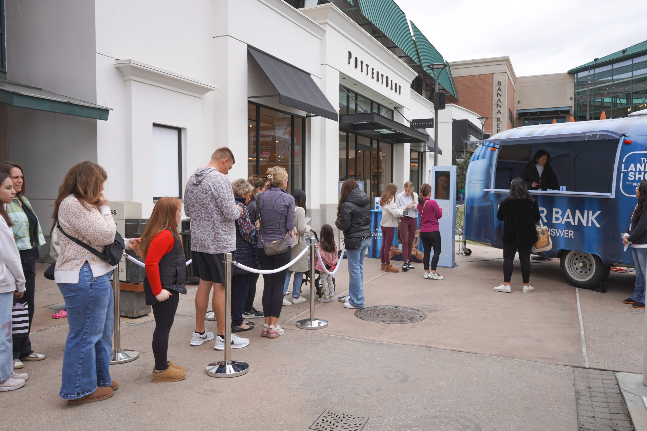 People, including adults and children, line up outside a store next to a blue promotional van.