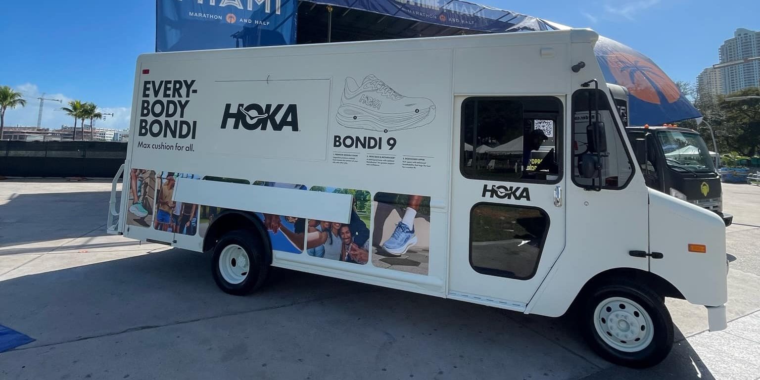White Hoka truck with running shoes, athletes, and "EVERY-BODY BONDI" and "BONDI 9" text on side.