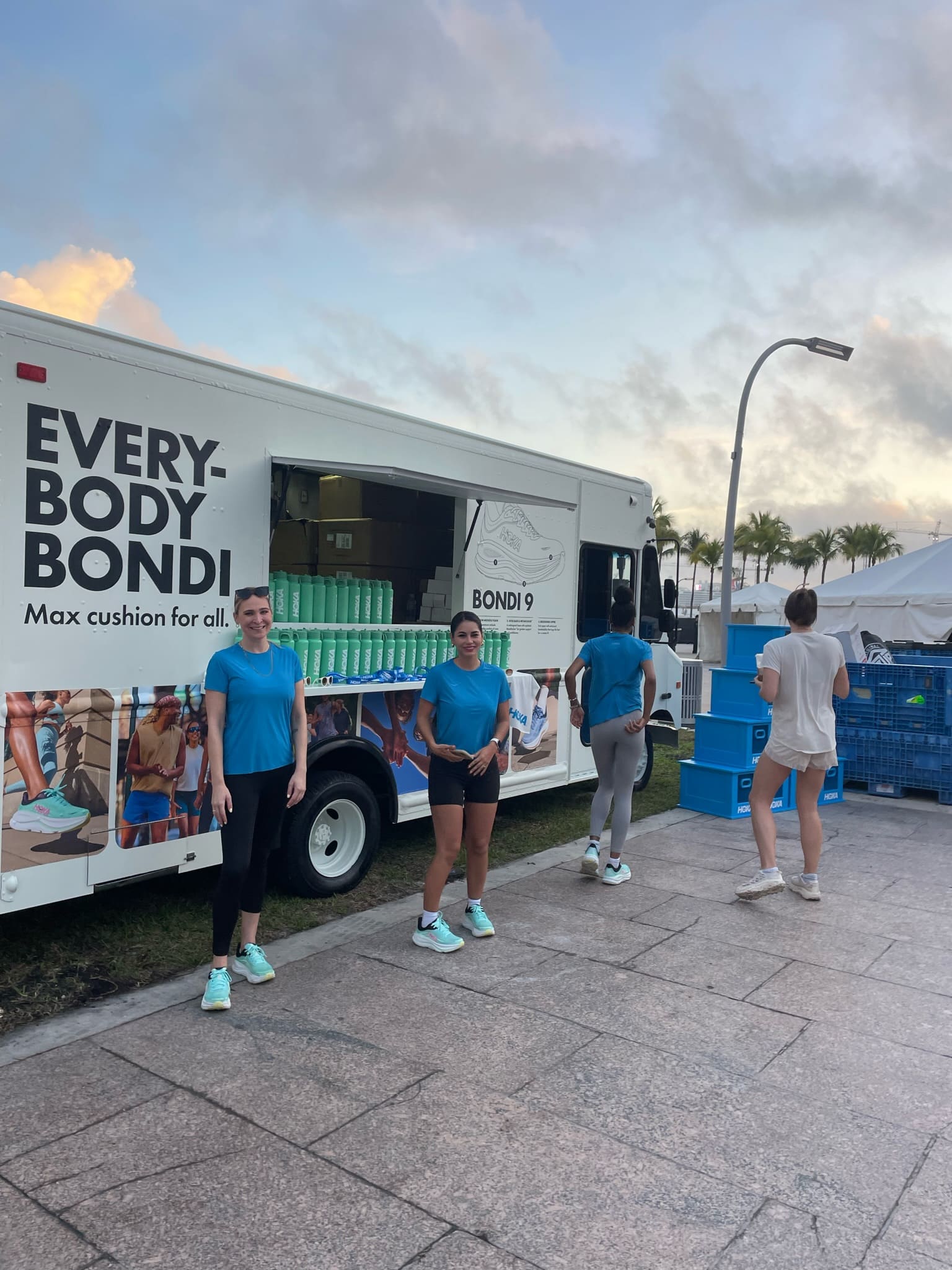 Four people in athletic wear stand by a white EVERYBODY BONDI truck at an outdoor event.