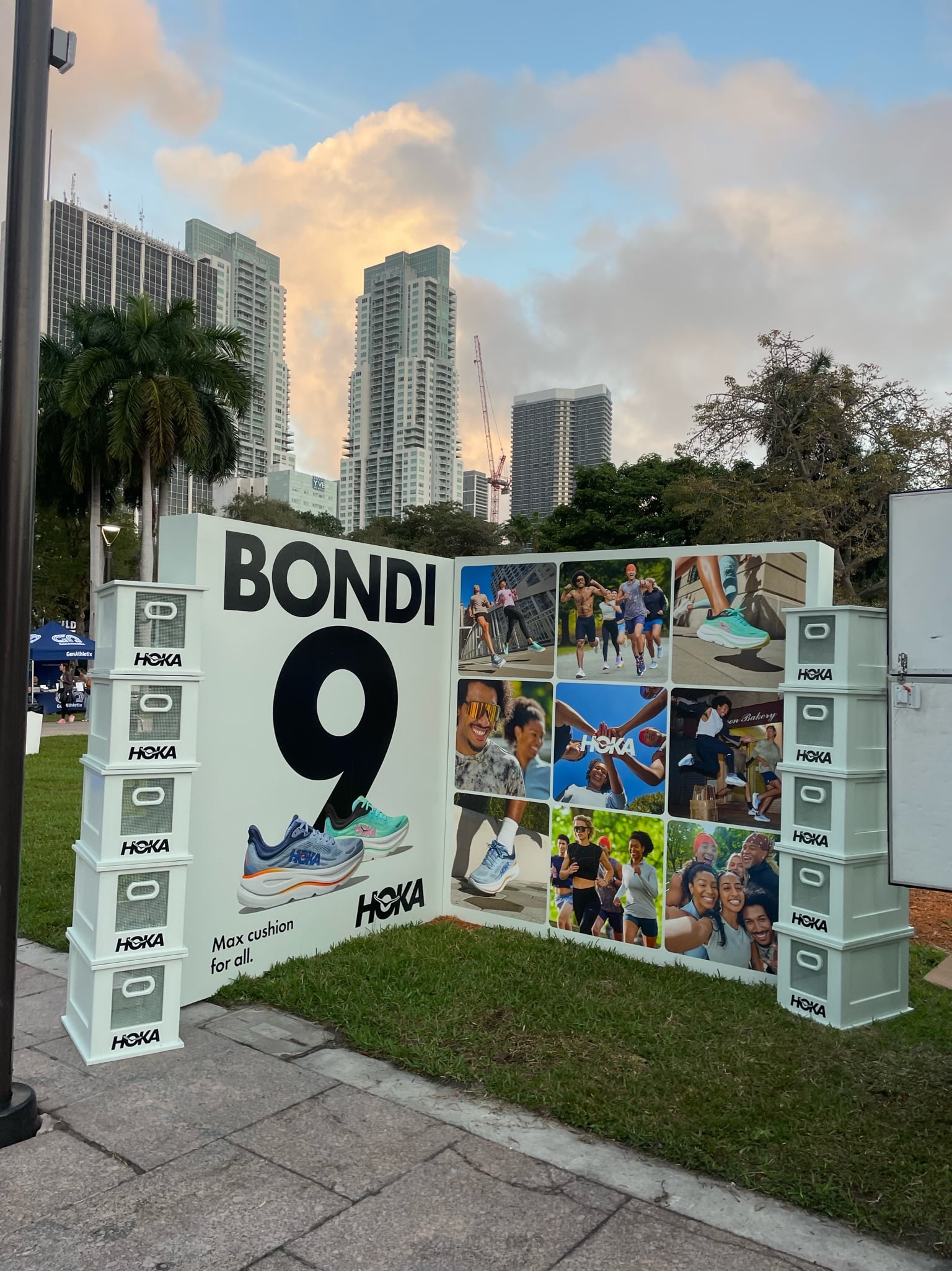 Hoka Bondi 9 outdoor display with stacked boxes, large sign, runners, buildings, and palm trees.