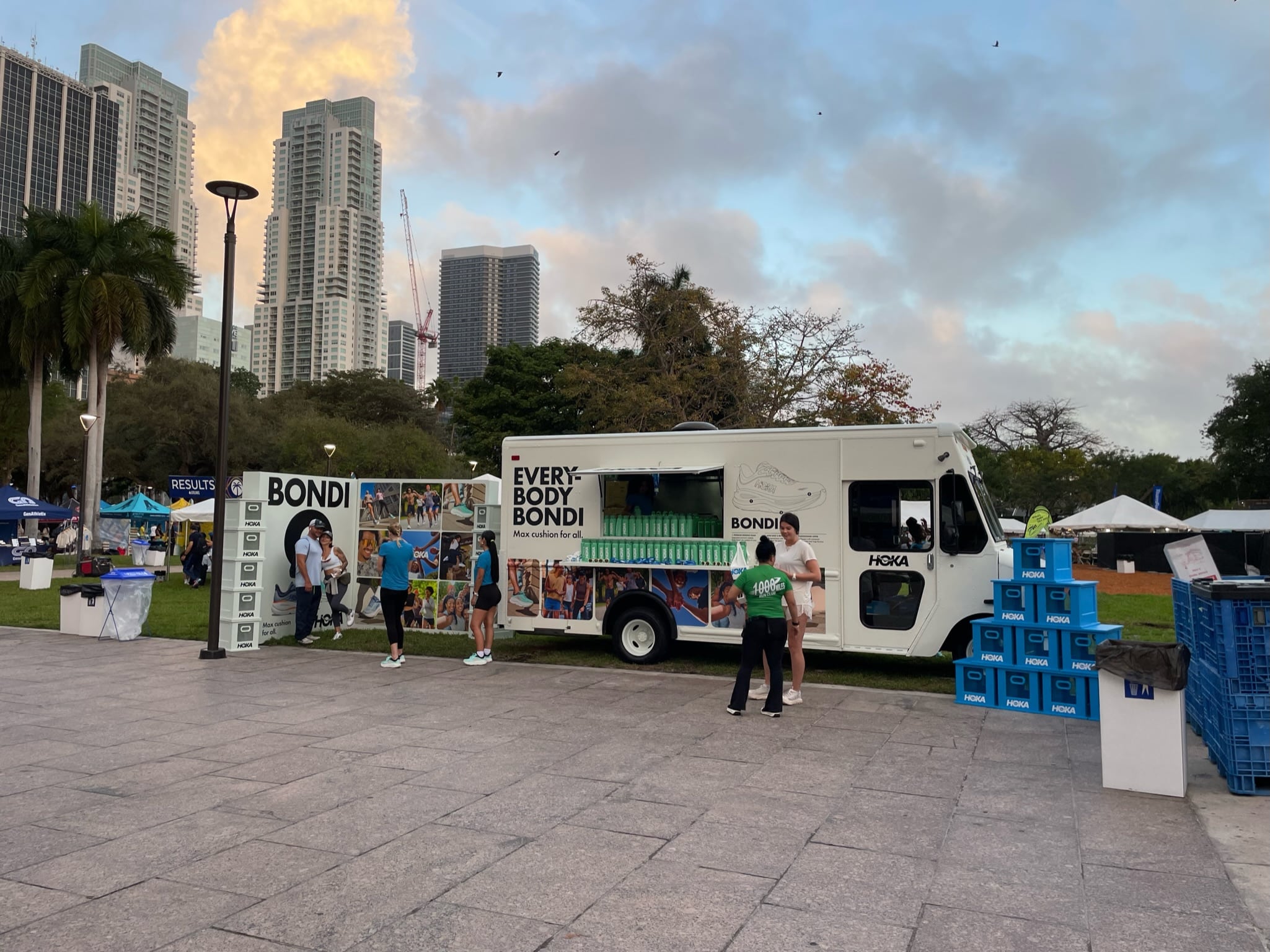 EVERYBODY BONDI food truck in a park with people, palm trees, buildings, and stacked crates nearby.