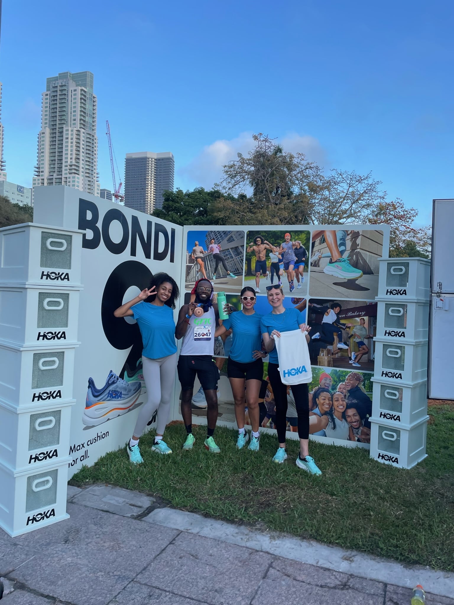 Four people in blue athletic wear stand smiling with HOKA gear before a BONDI shoe backdrop.