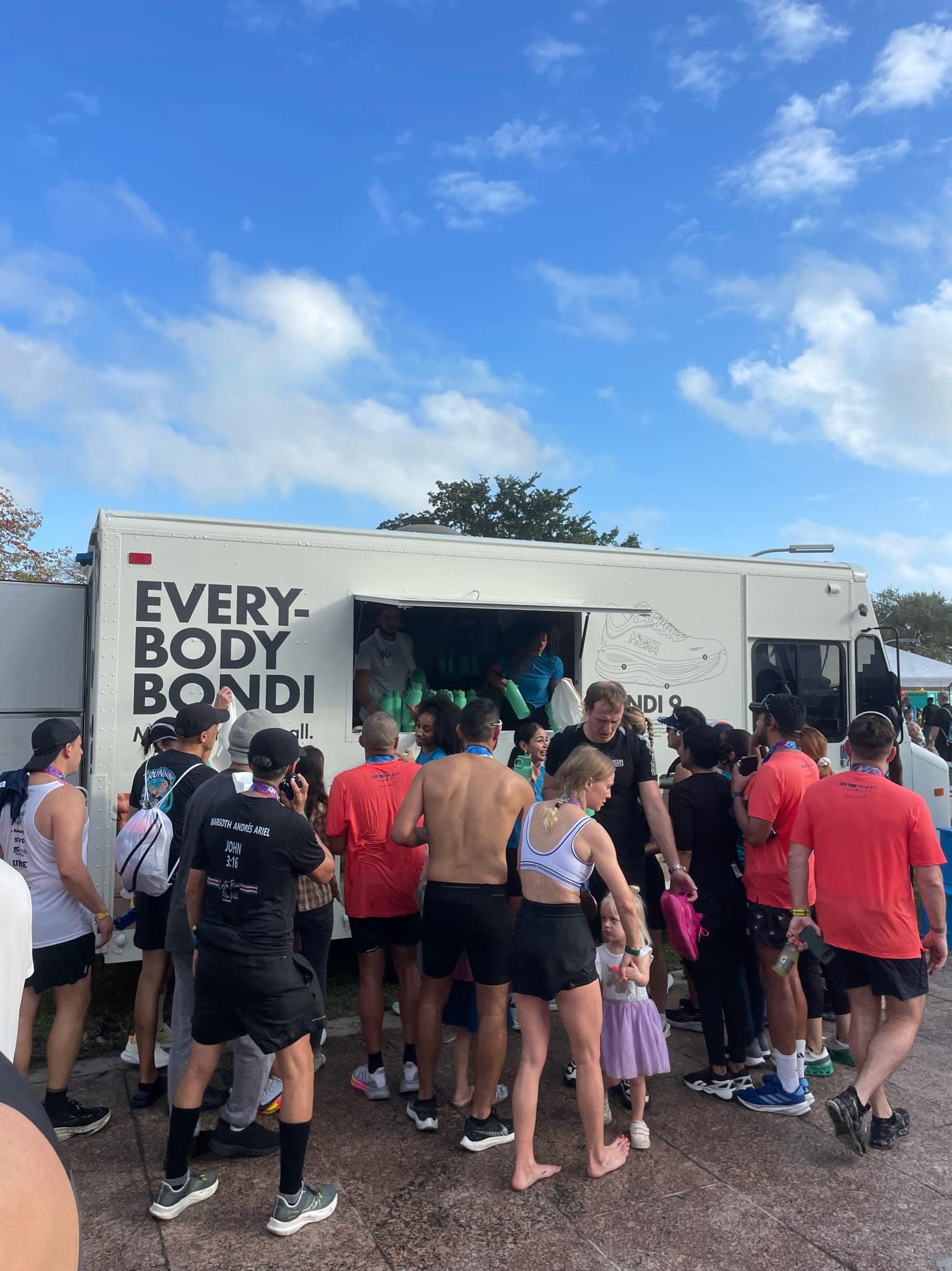 People in athletic wear gather near a white EVERYBODY BONDI truck; a child stands in front.