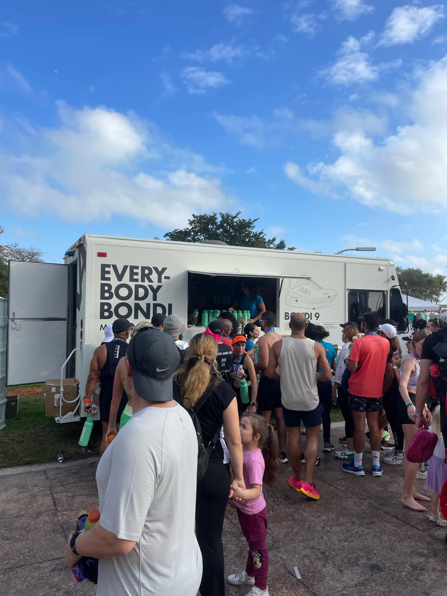 People, adults and children, line up outside a white truck labeled EVERYBODY BONDI under blue sky.