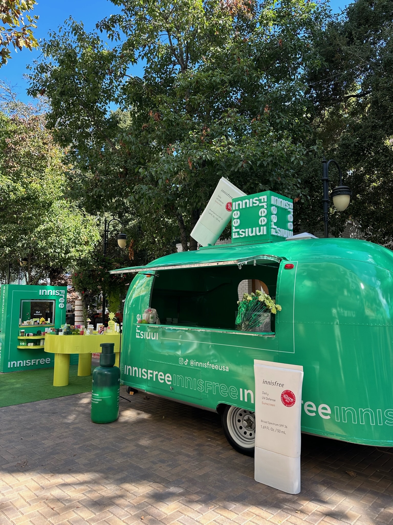 Green Innisfree airstream trailer outdoors with skincare displays and samples by trees.