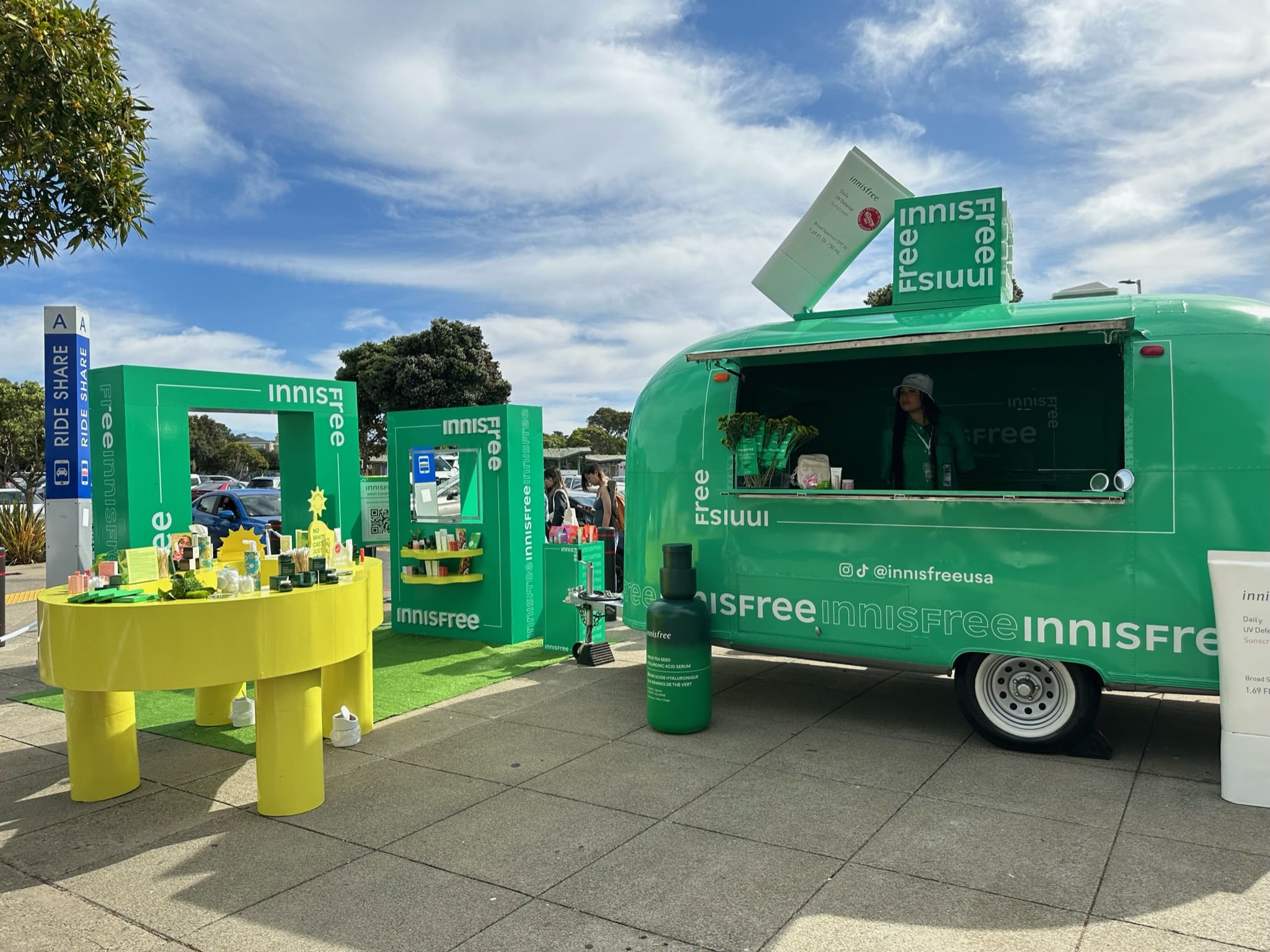 Green Innisfree pop-up trailer with skincare products outside; a person stands inside.