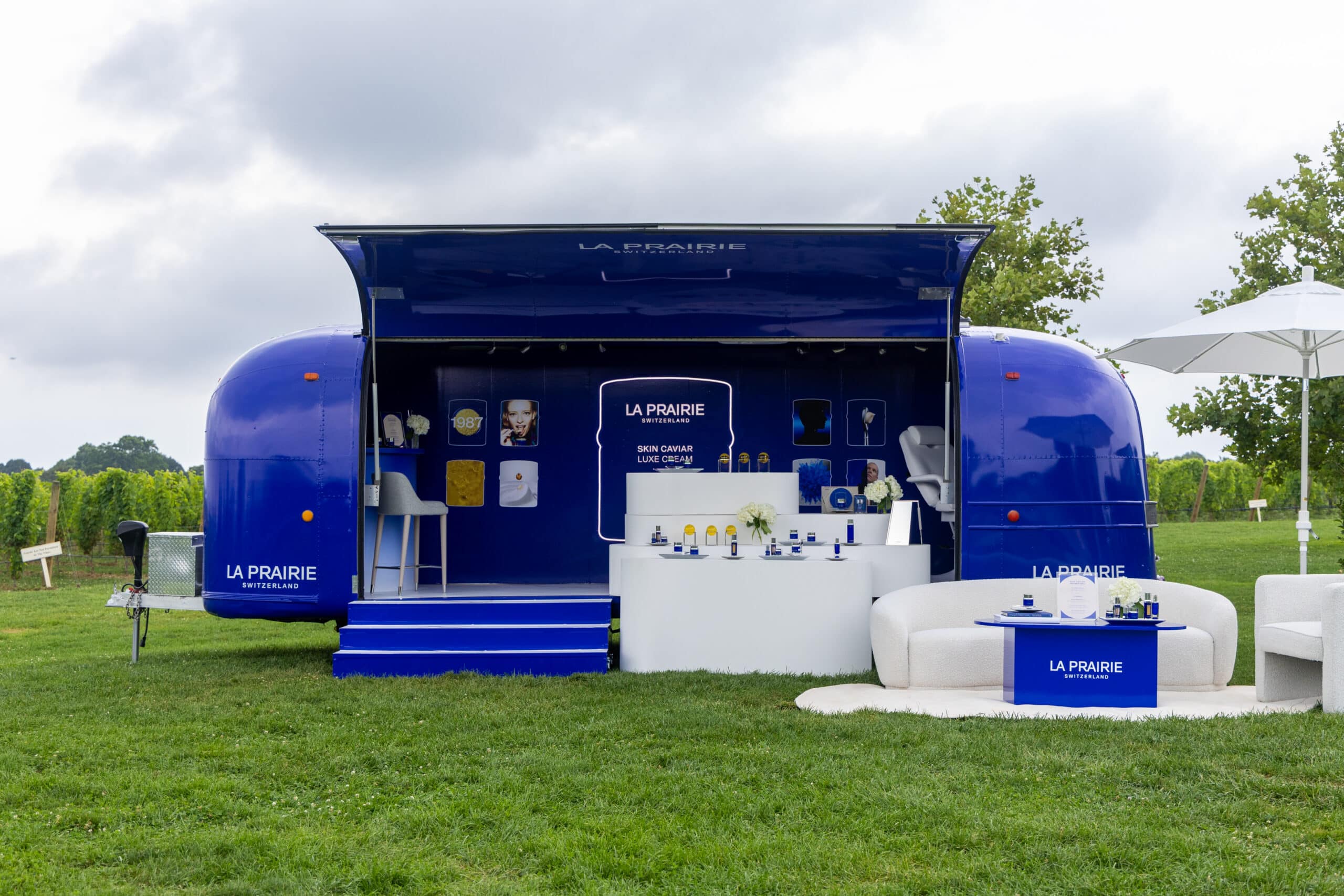 La Prairie Airstream trailer on grass with skincare displays, white counters, and outdoor furniture.