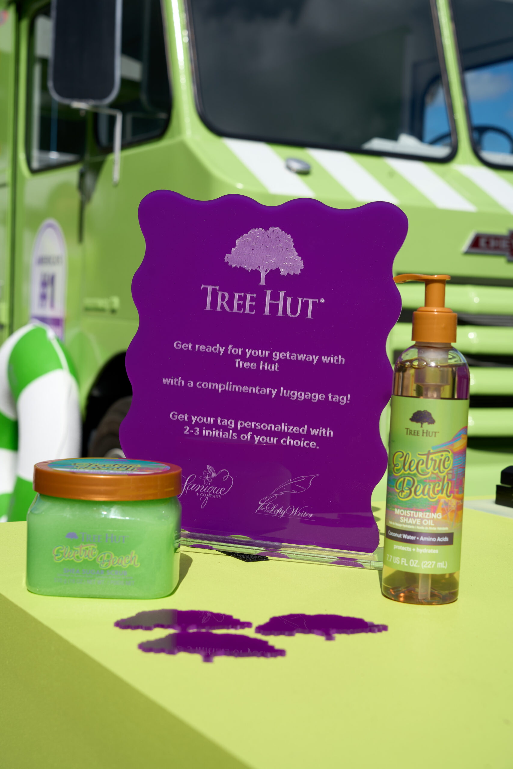 Tree Hut Electric Punch lotion jar and pump bottle, promo sign, and green truck in back.