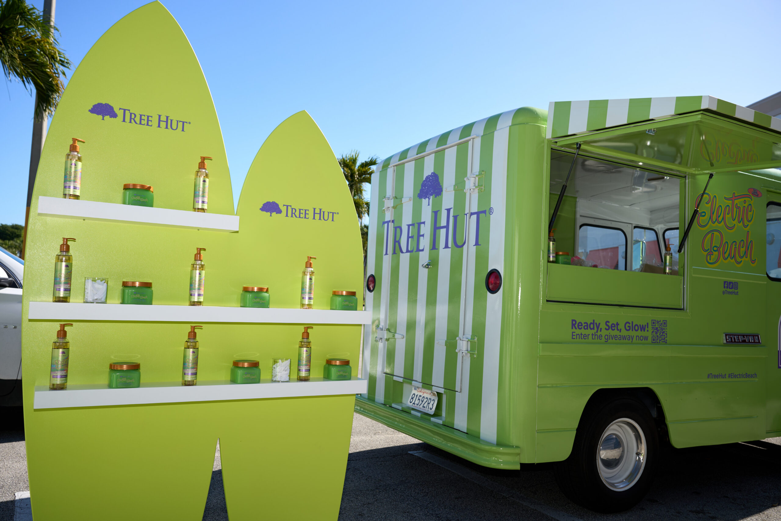 Tree Hut truck parked by a display shelf with skincare bottles; palm trees in the background.