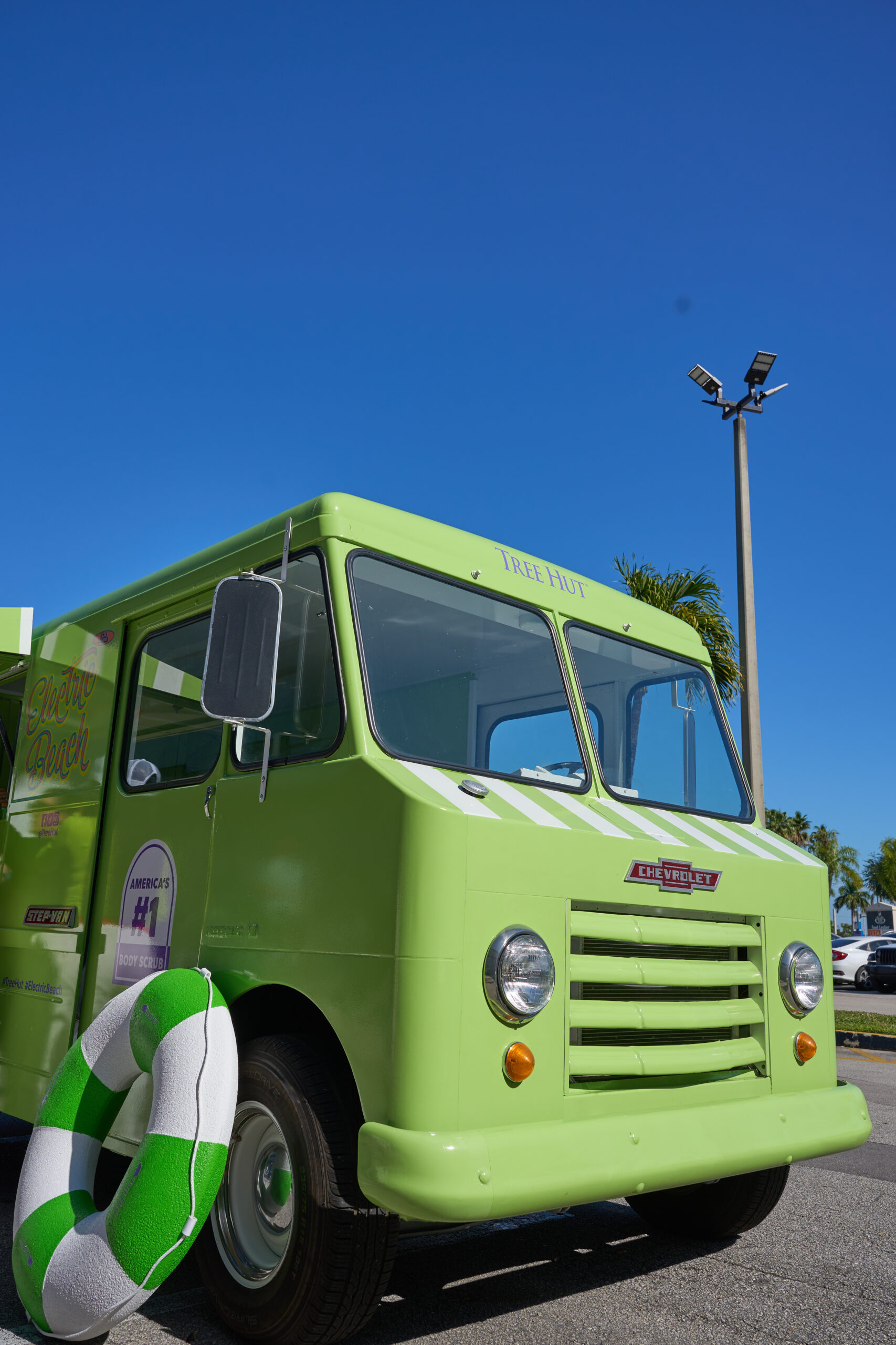 Light green vintage Chevrolet step van with a green and white pool float by the bumper.
