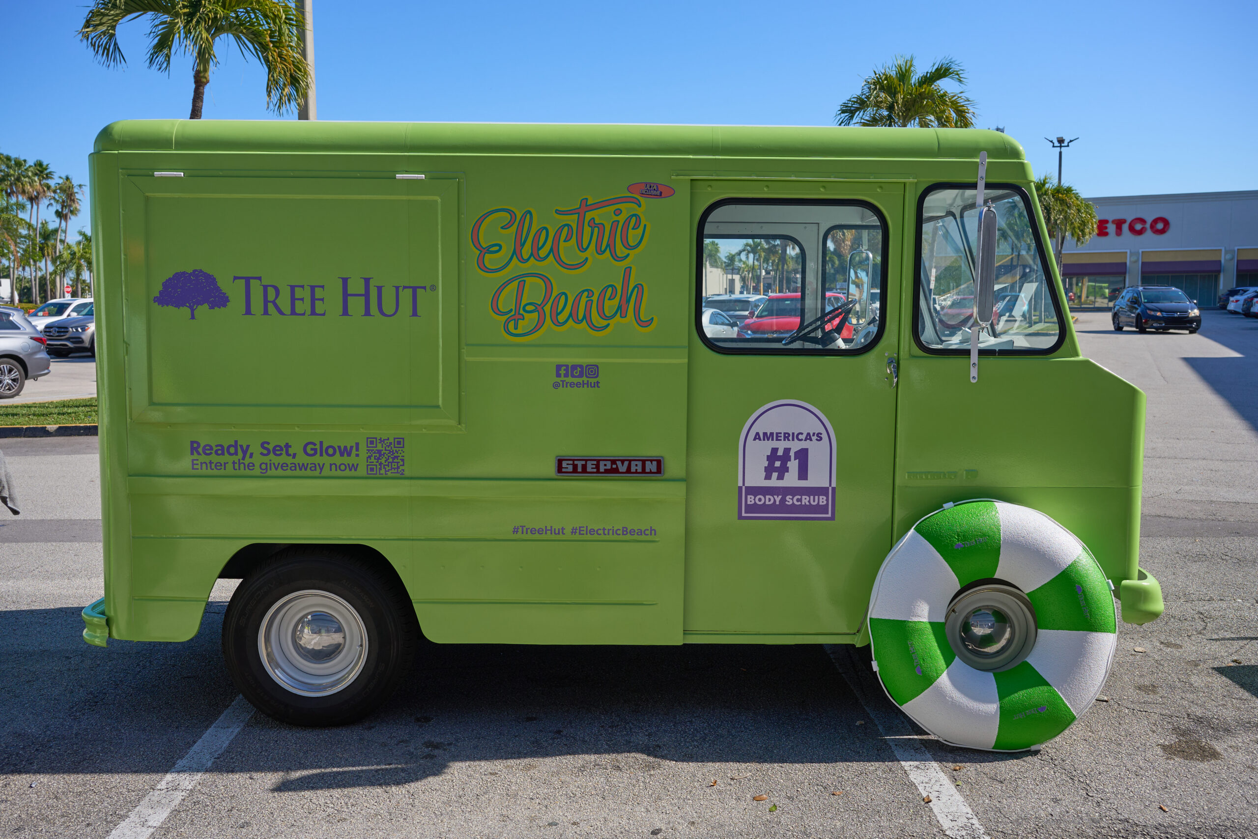 Green Tree Hut van with Electric Beach branding, front wheel lifebuoy, palm trees in background.