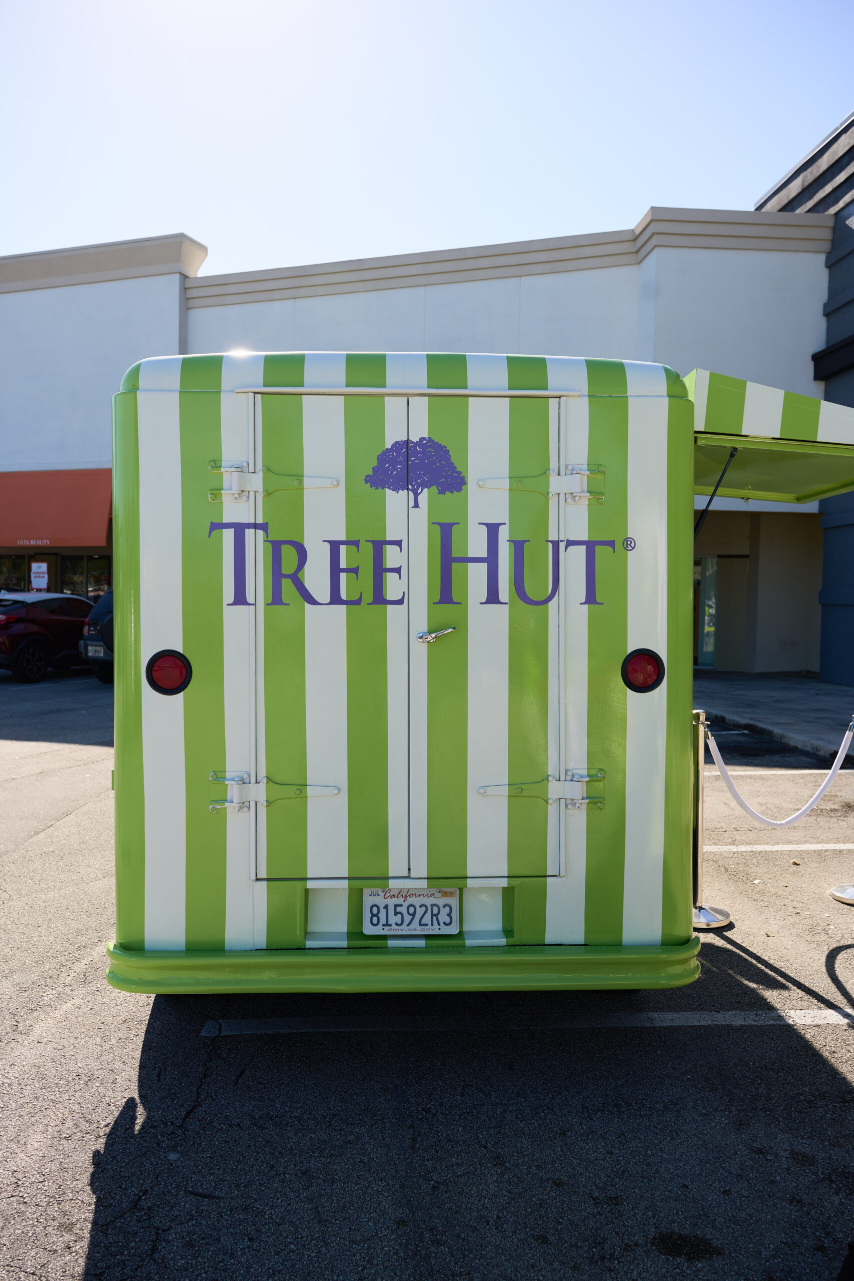 Back of green and white striped TREE HUT food truck with purple tree logo in a parking lot.