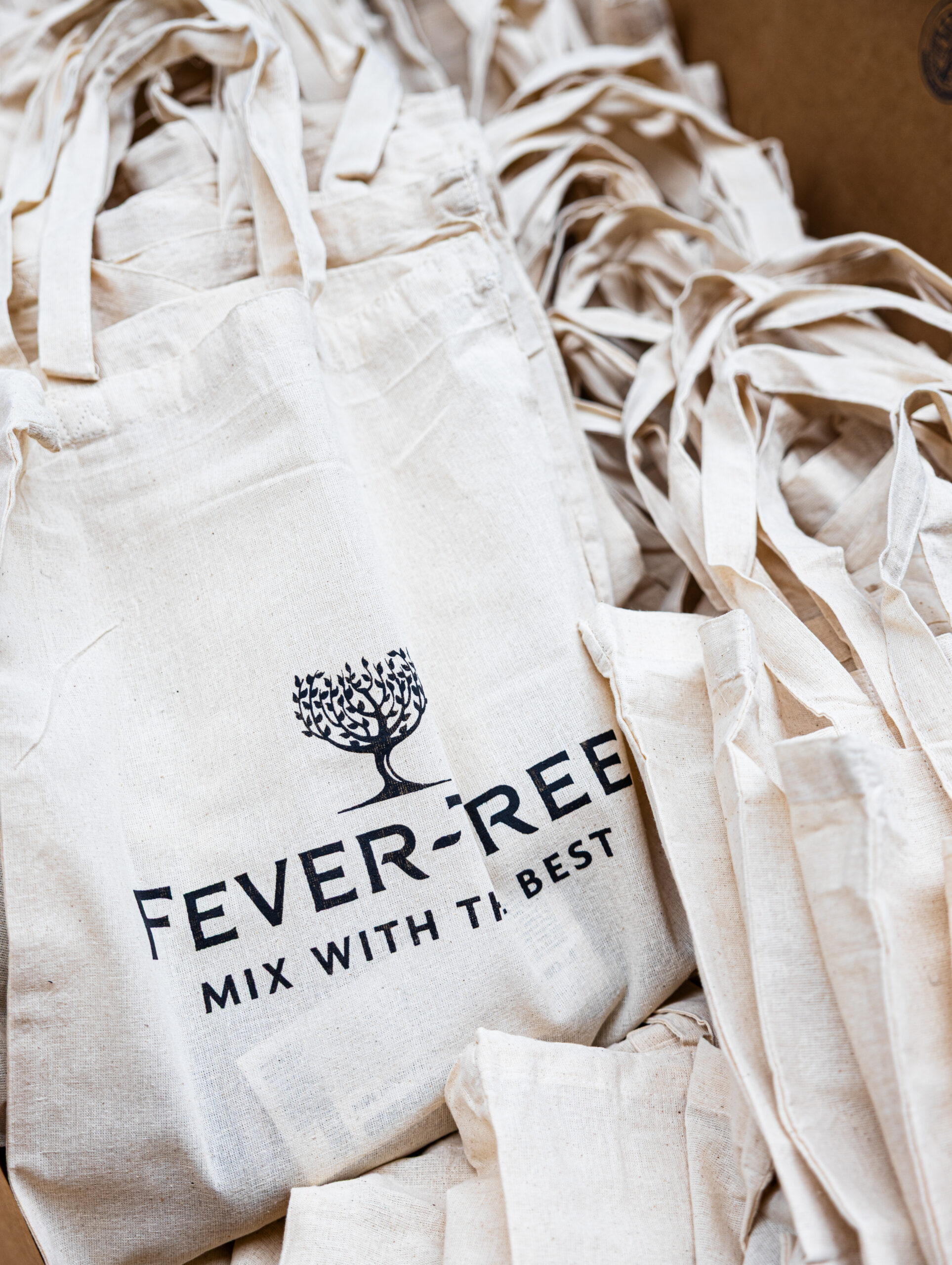 Cream-colored tote bags with Fever-Tree logo, "Mix With The Best" slogan, and a tree graphic.