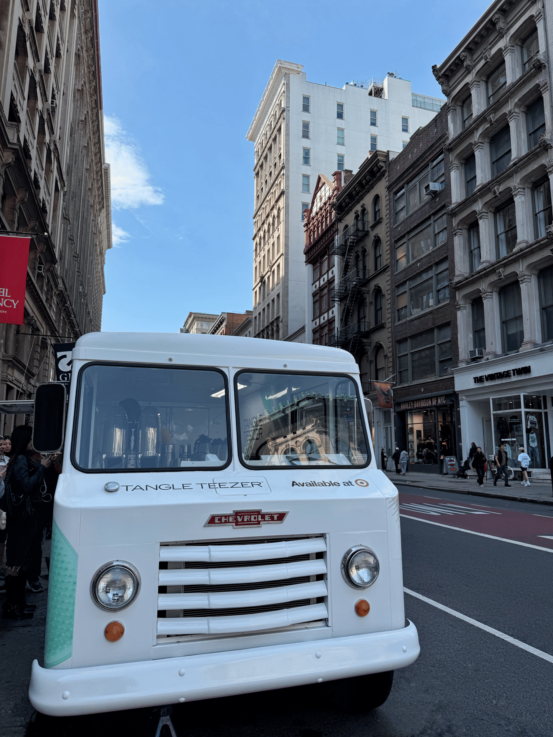 A white Tangle Teezer food truck is parked on a city street with people nearby.
