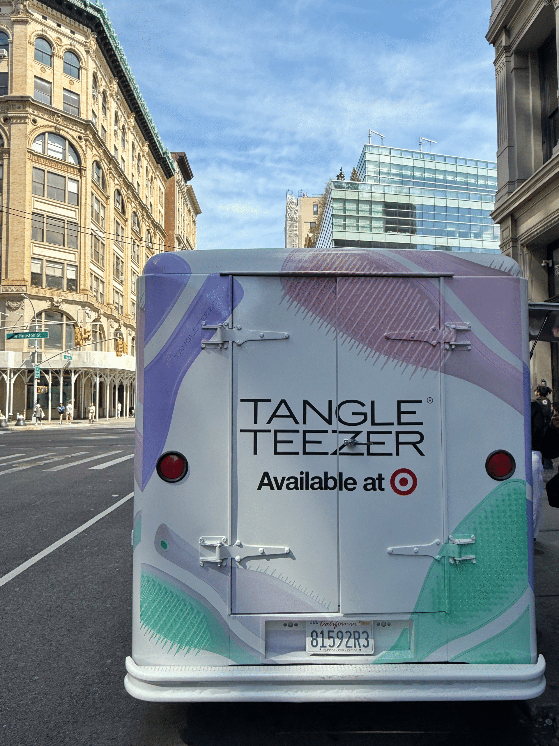 A delivery van with “TANGLE TEEZER Available at Target” on the back is parked on a city street.