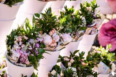 White buckets filled with assorted pastel pink and purple flowers and green foliage, arranged closely together in rows, creating a vibrant and fresh floral display.