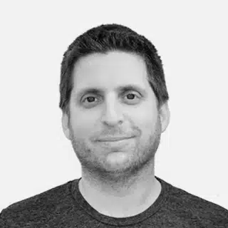 A man with short dark hair and light stubble is smiling slightly, facing forward. He is wearing a dark crew-neck shirt against a plain, light background—ideal for promoting experiential marketing trucks.
