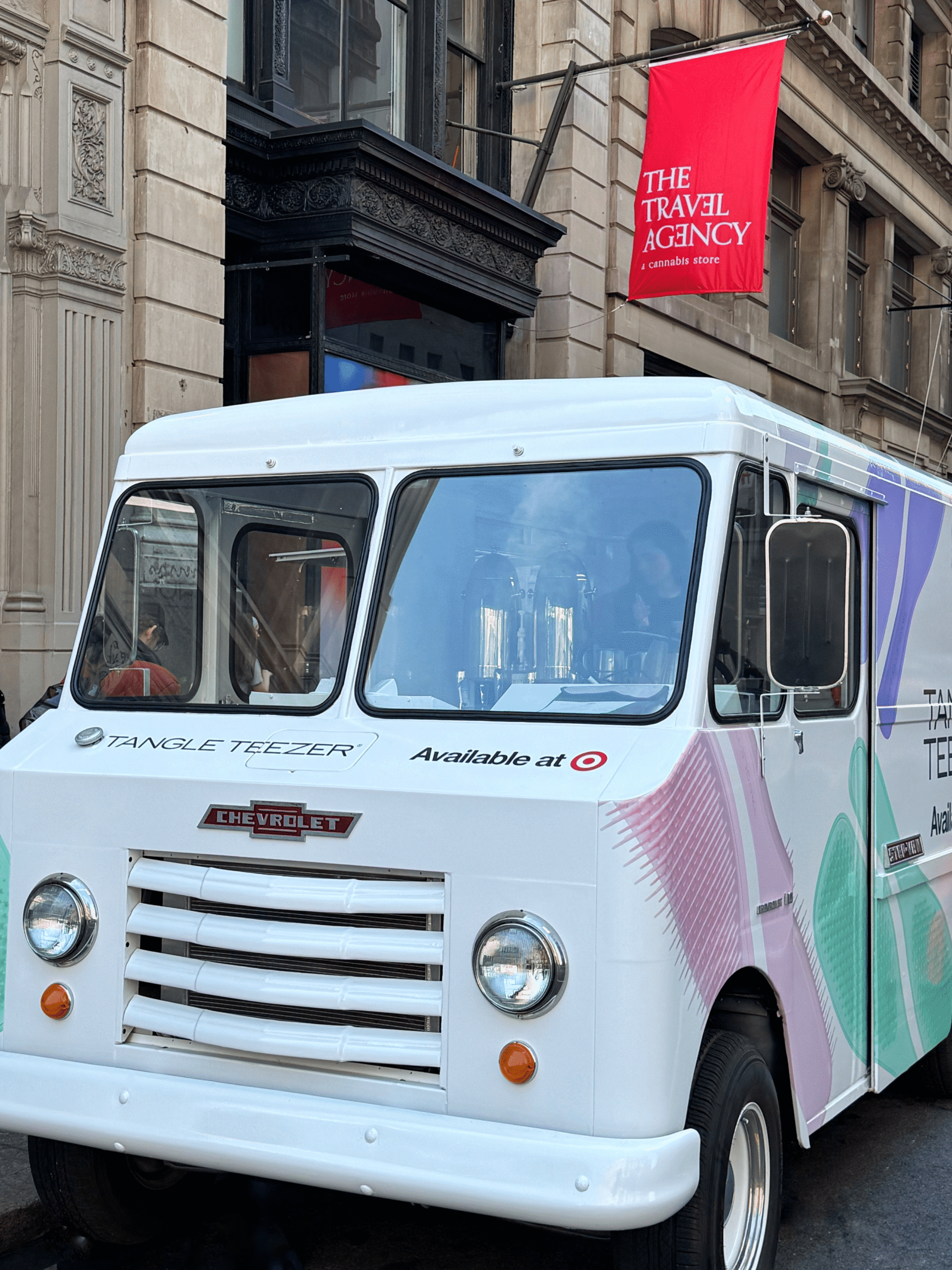 Tangle Teezer promo truck parked on city street, red Travel Agency banner in background.