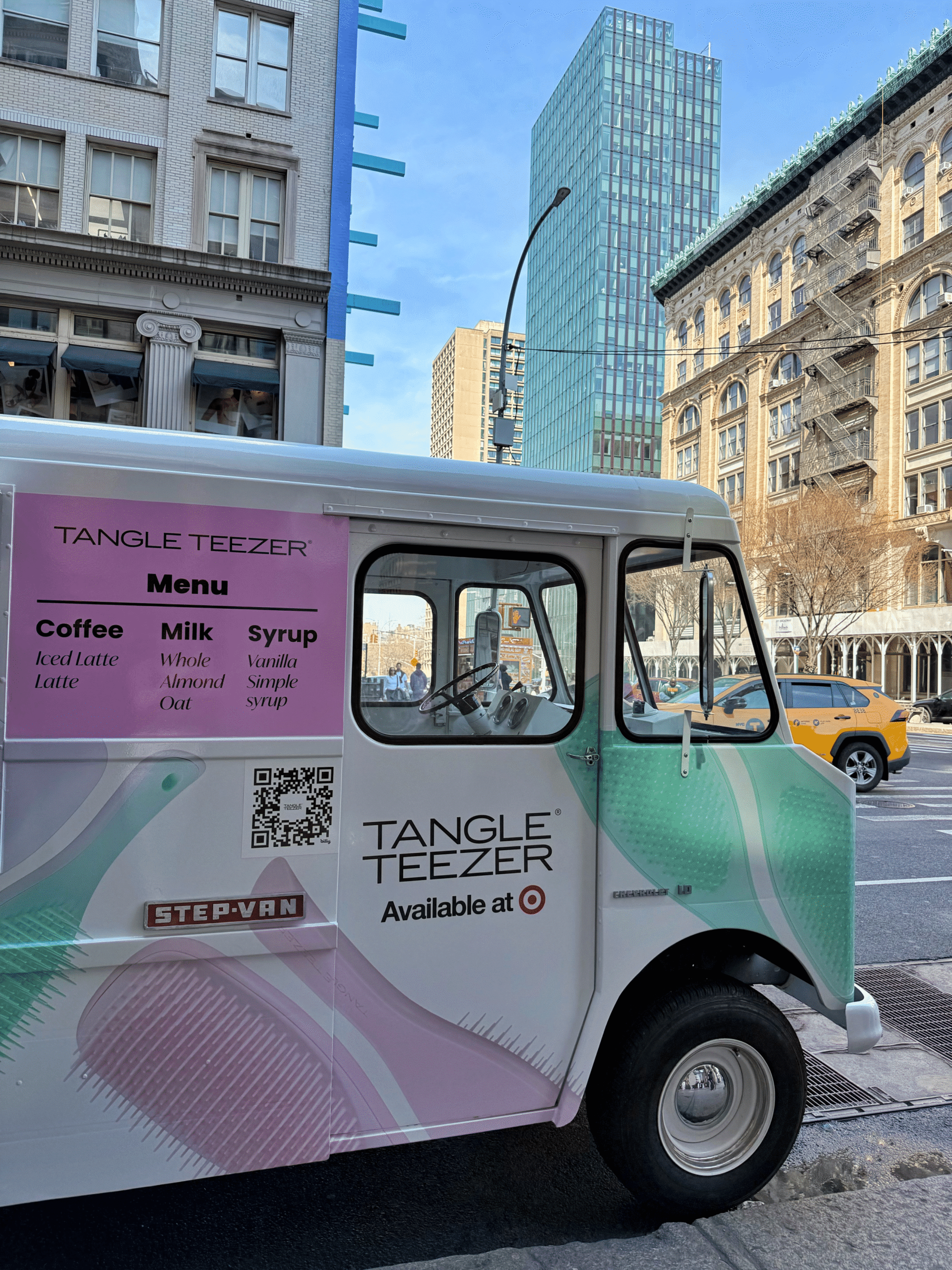 Tangle Teezer van with a coffee menu parked on a city street; buildings and yellow taxi in back.