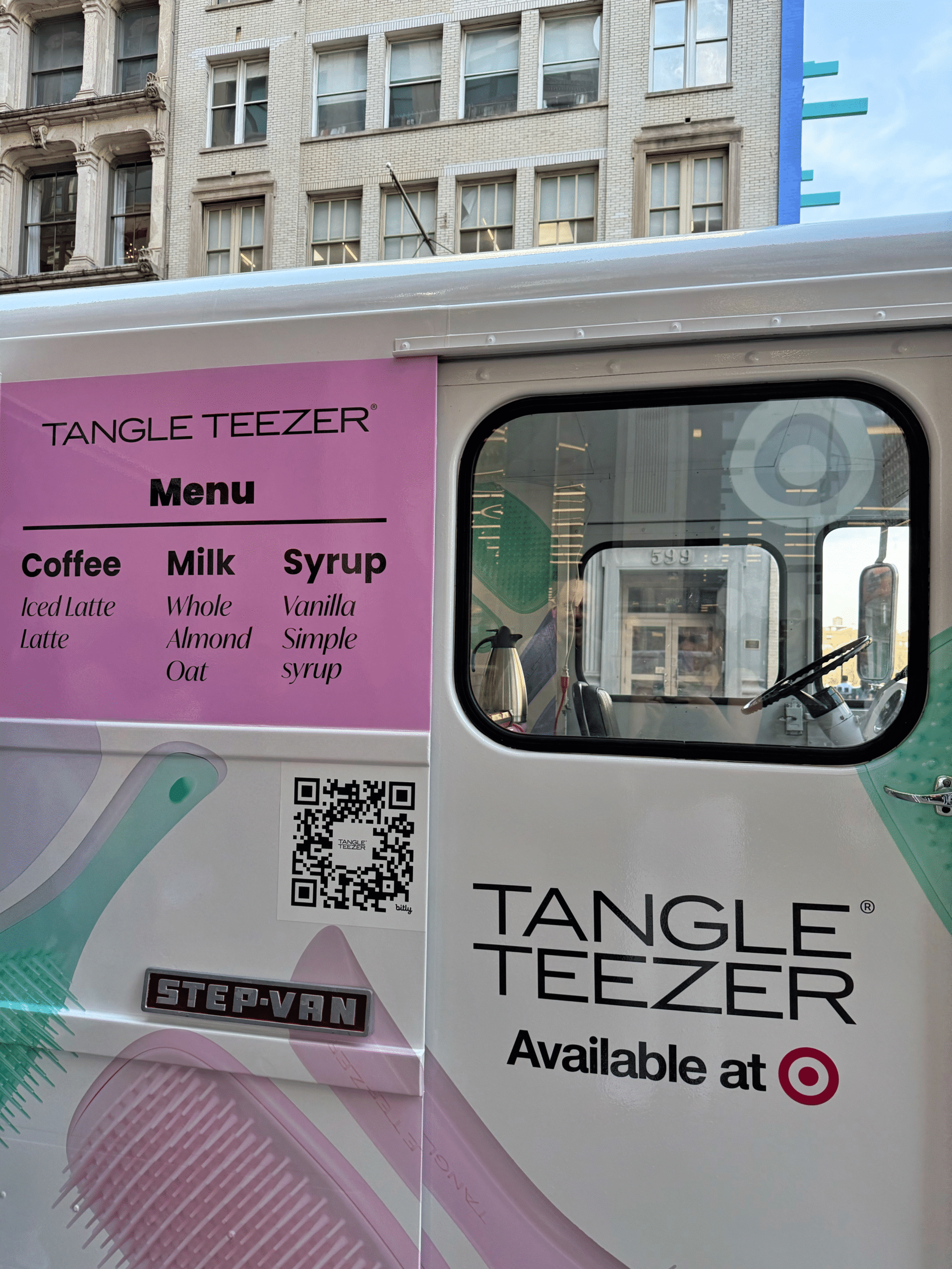 Tangle Teezer van with coffee menu, QR code, Target logo, and city buildings reflected in window.