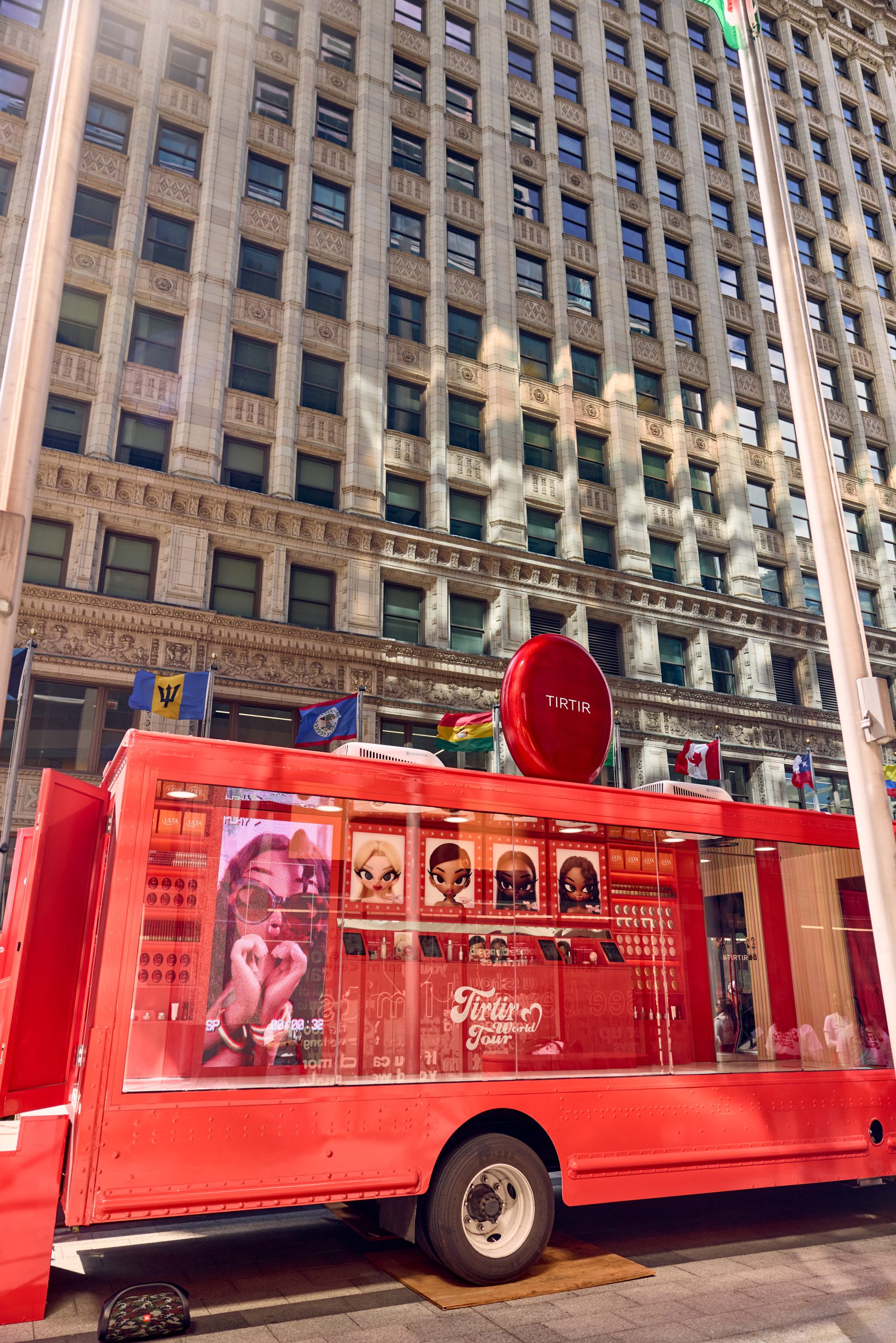Red TIRTIR food truck parked on city street near tall building with many windows and flags.