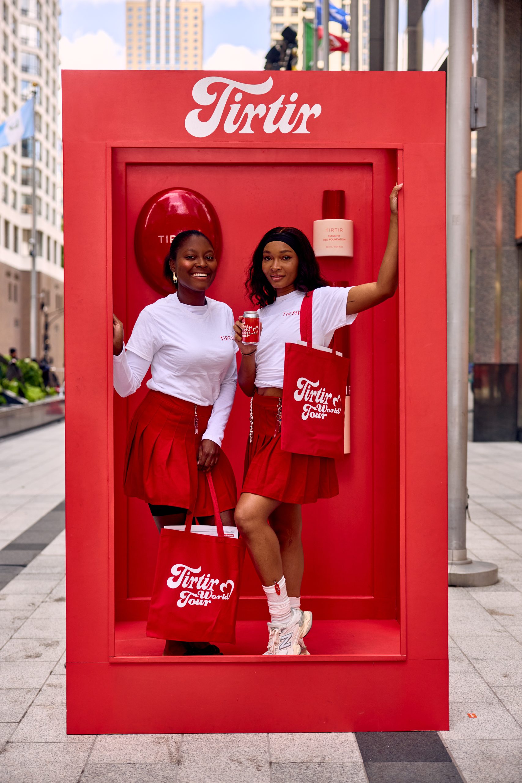 Two women in matching white shirts and red skirts stand in a red “Tirtir” photo booth frame.