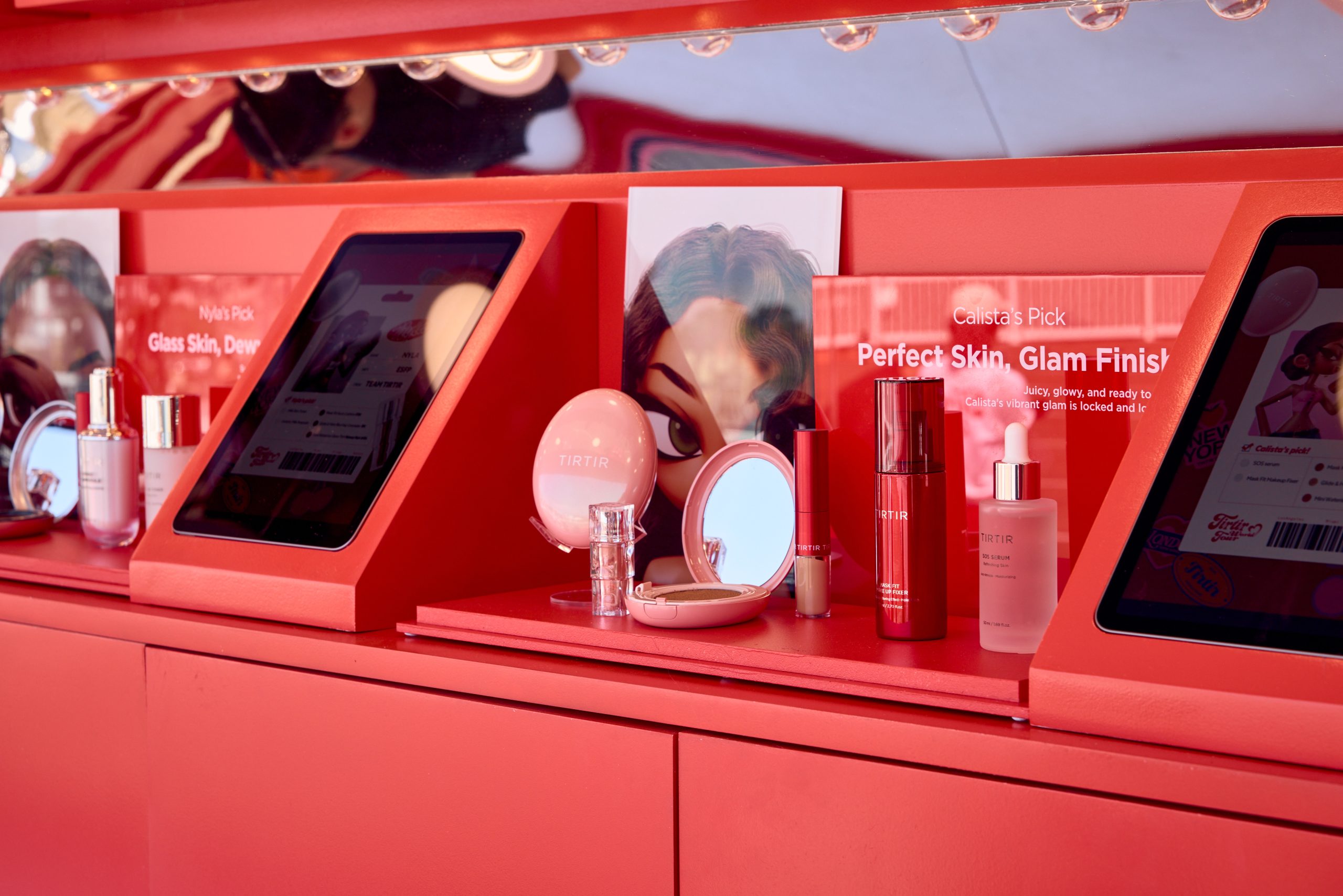 Skincare and makeup products on a pink shelf with screens and part of a woman's face behind them.