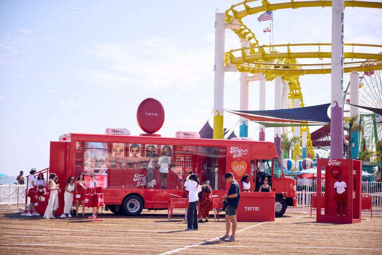 Red TRTR beauty truck parked on boardwalk with a line of people; roller coaster in background.
