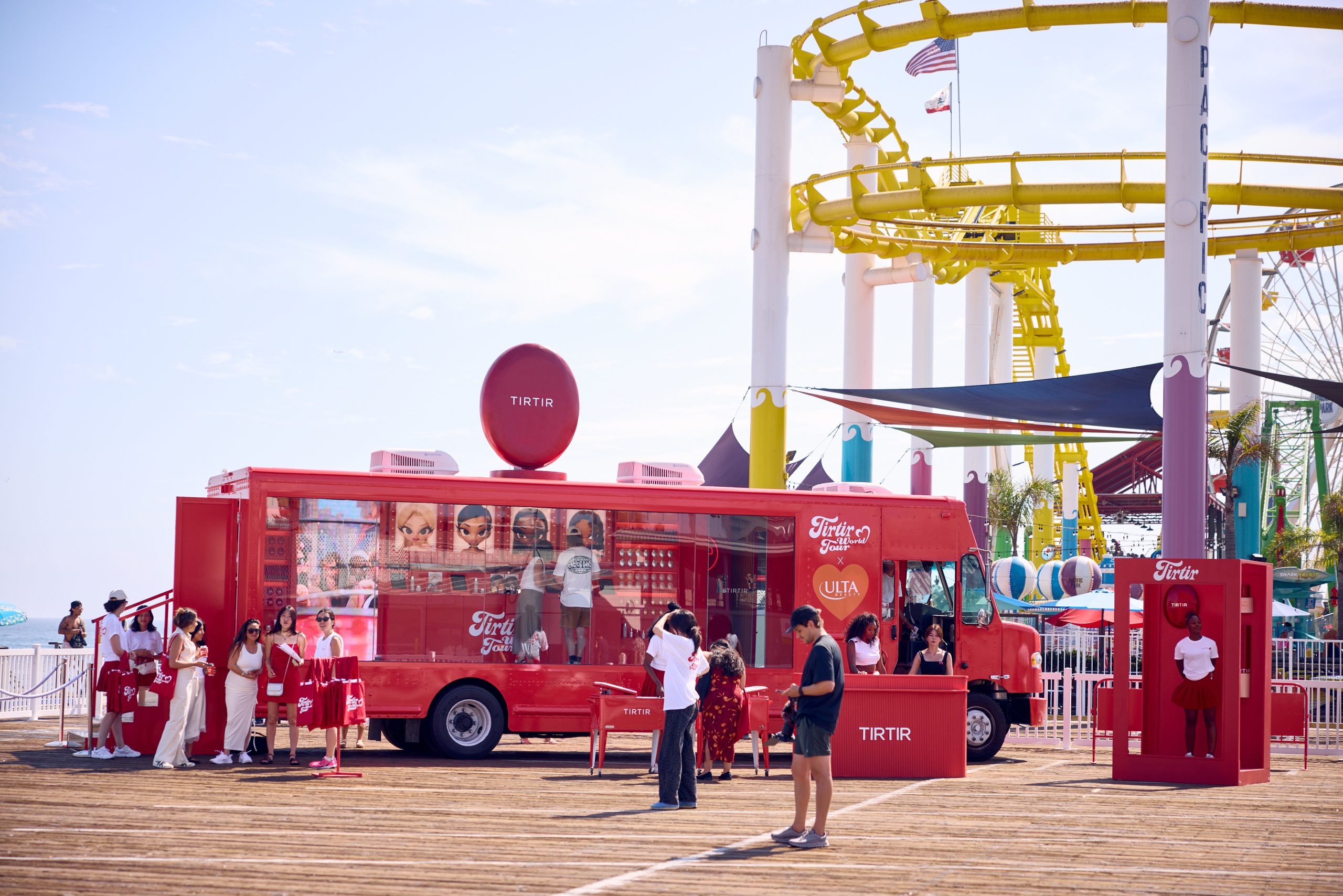 Red TRTR beauty truck parked on boardwalk with a line of people; roller coaster in background.