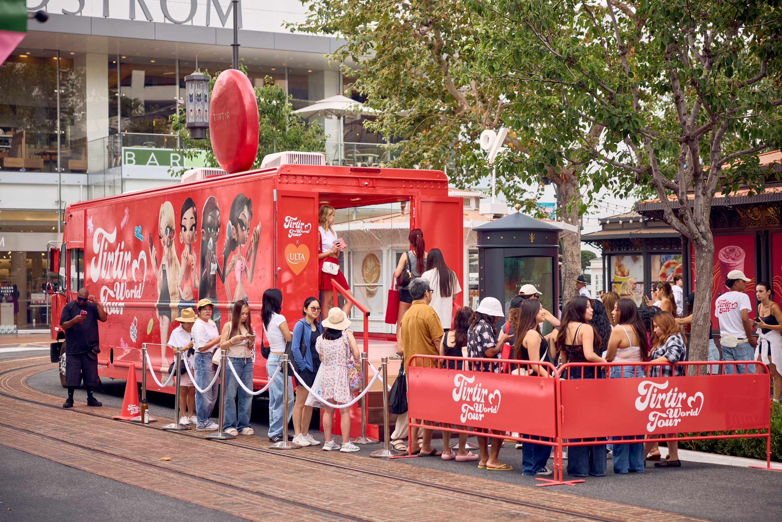 People line up outside a red beauty pop-up truck with lip illustrations at a shopping area.