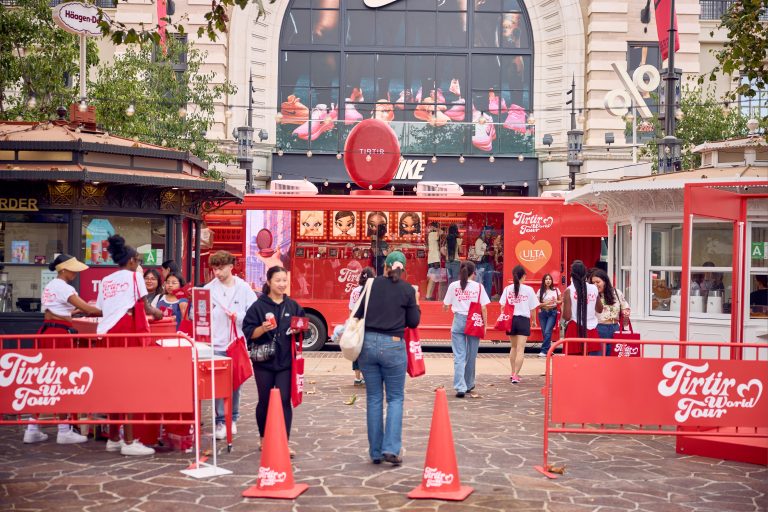 Red Tirtir World Tour bus outside Nike store with people receiving items from staff.