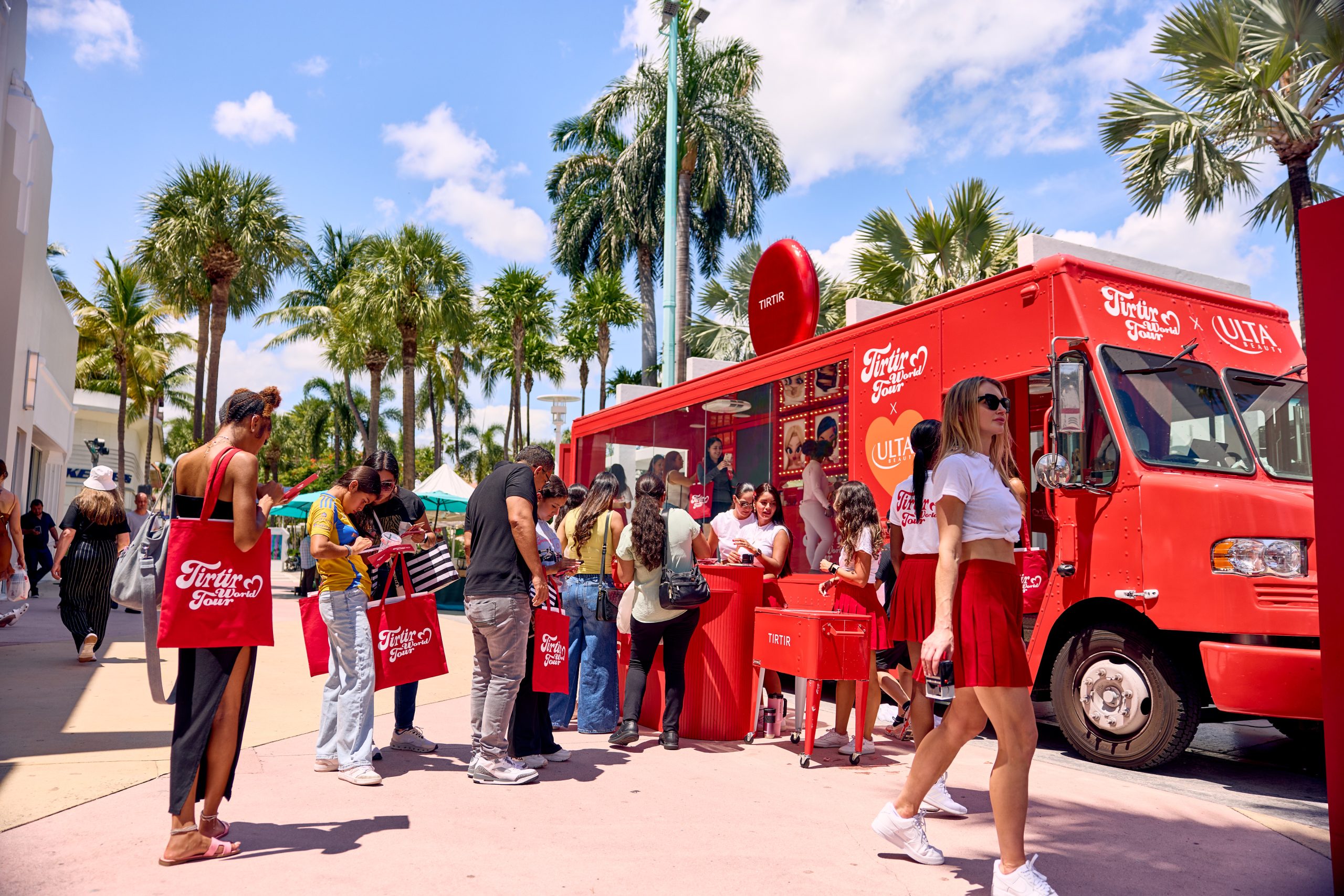 People gather by a red First Aid Squad food truck under palm trees; a woman in red walks by.