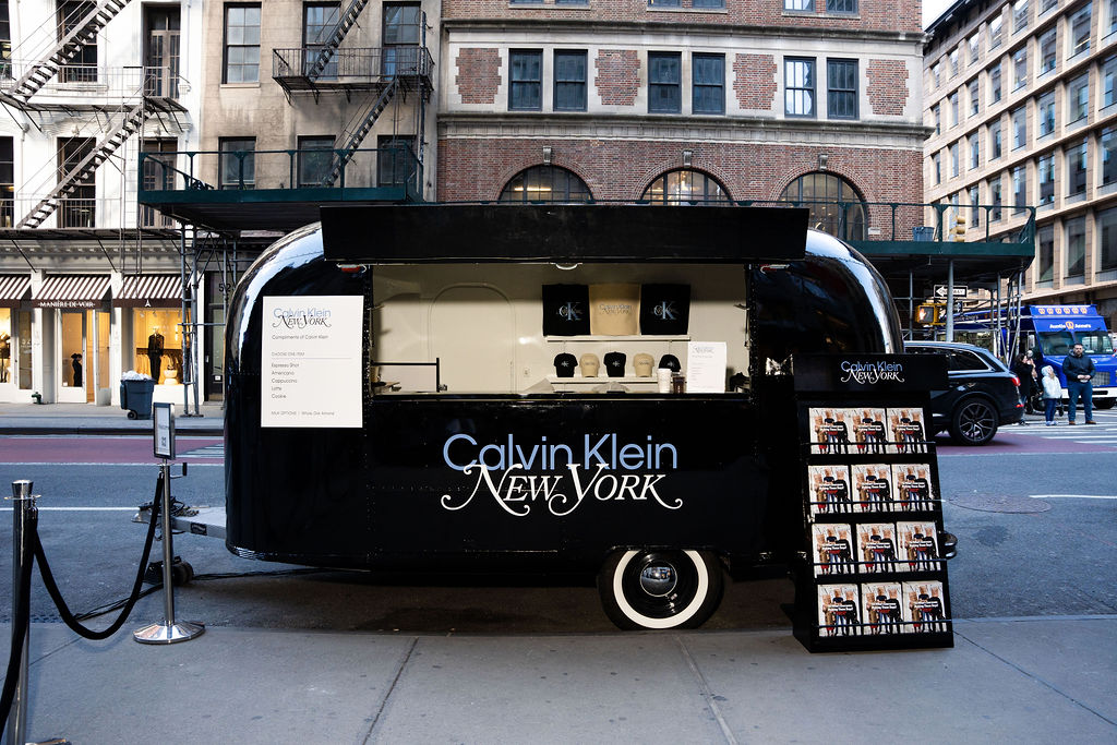 Calvin Klein New York pop-up trailer on city street with displays, sign, and a counter window.
