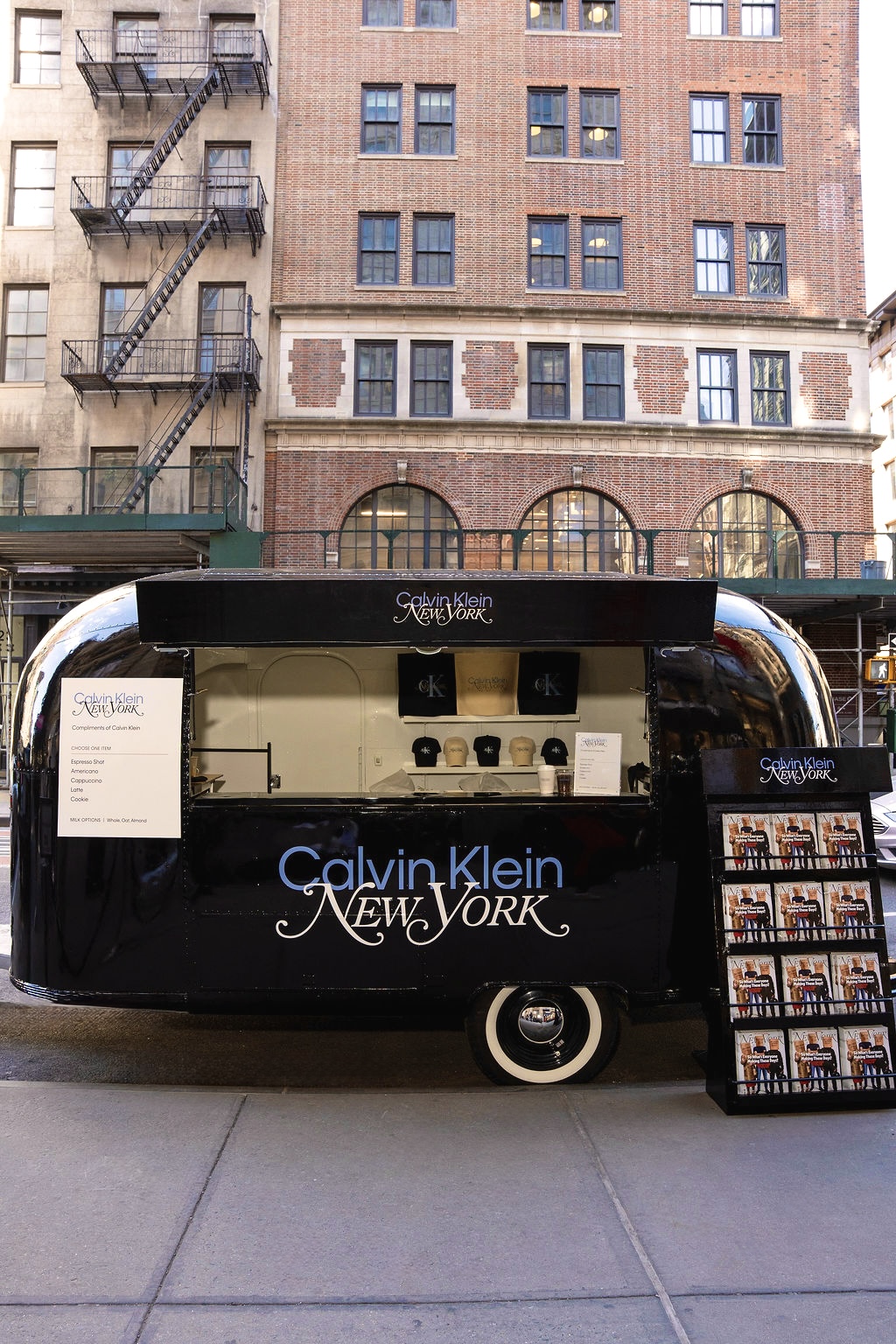 Black Calvin Klein New York food truck with service window and display stand on a city street.