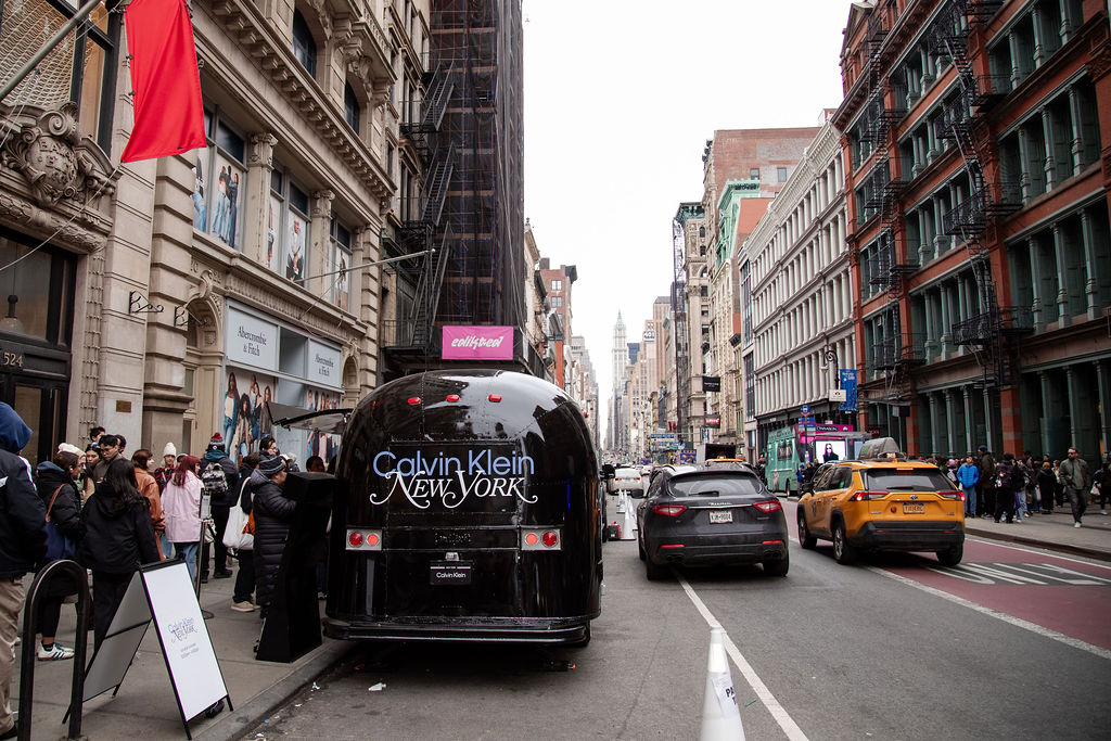 People walk past a black Calvin Klein trailer on a New York City street with cars and taxis.