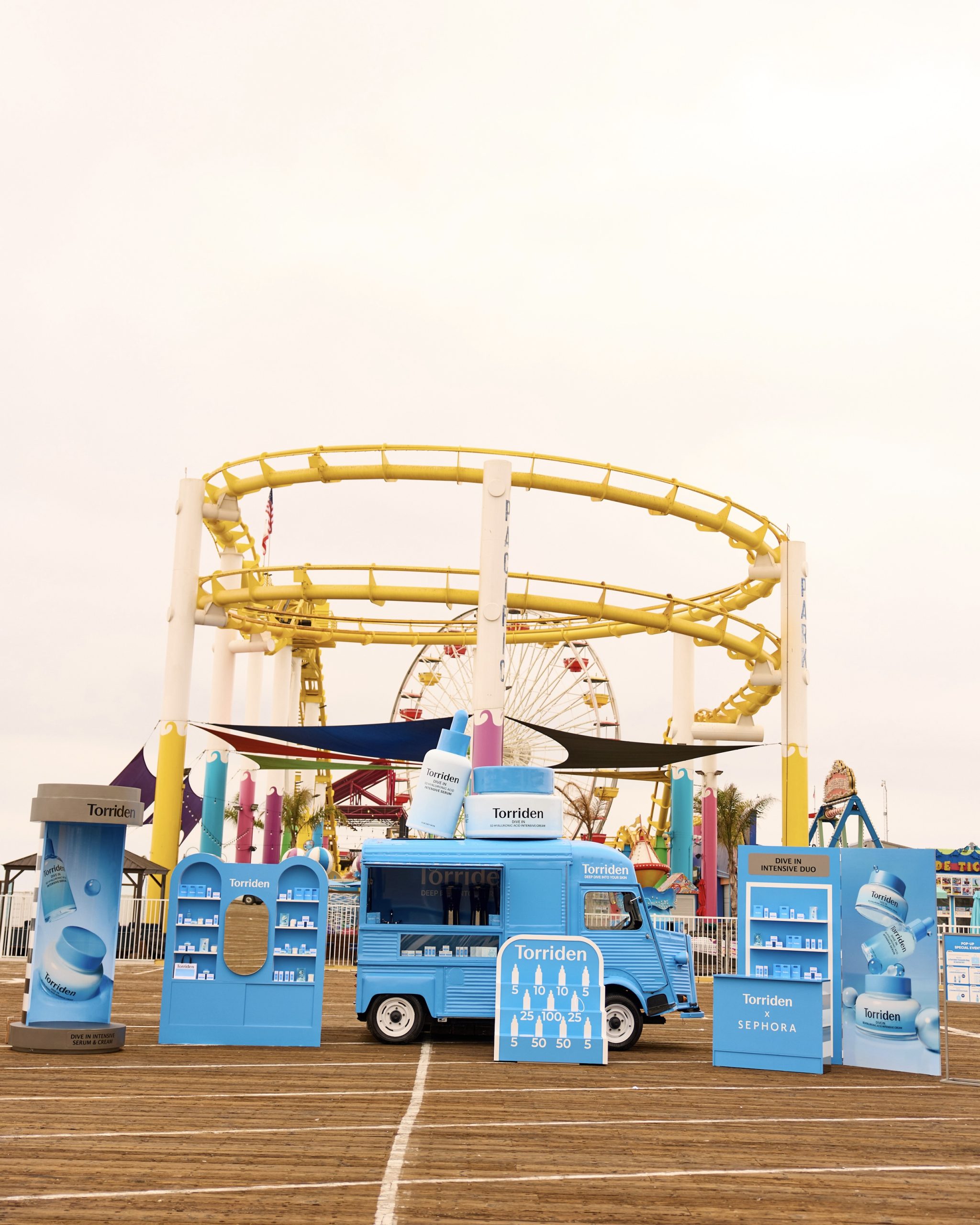 Blue Torriden truck and products on a boardwalk with a yellow roller coaster and Ferris wheel behind.