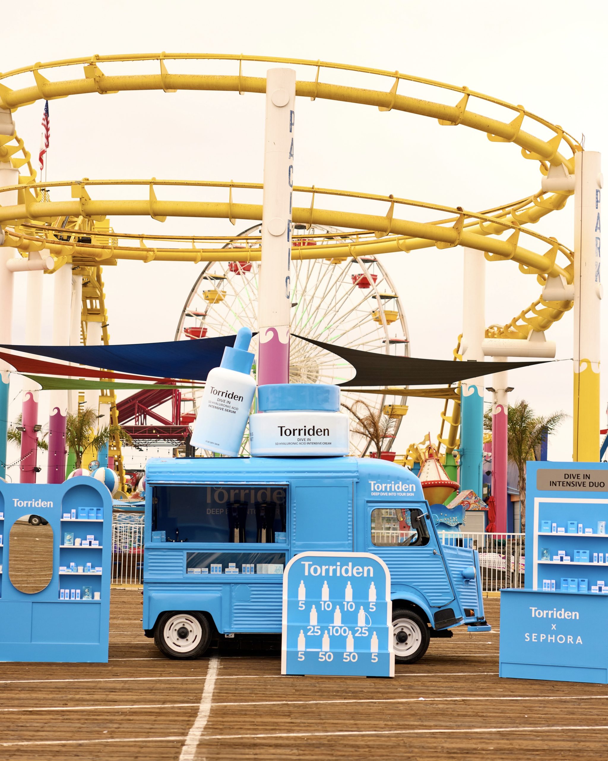 Blue Torriden promo truck with large product models at a fairground; Ferris wheel behind.