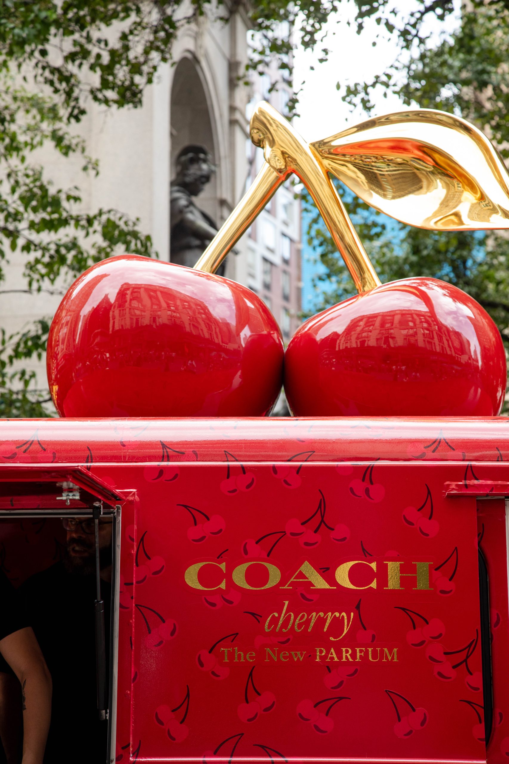 Red Coach Cherry perfume truck with large red cherries on top, parked on a city street.