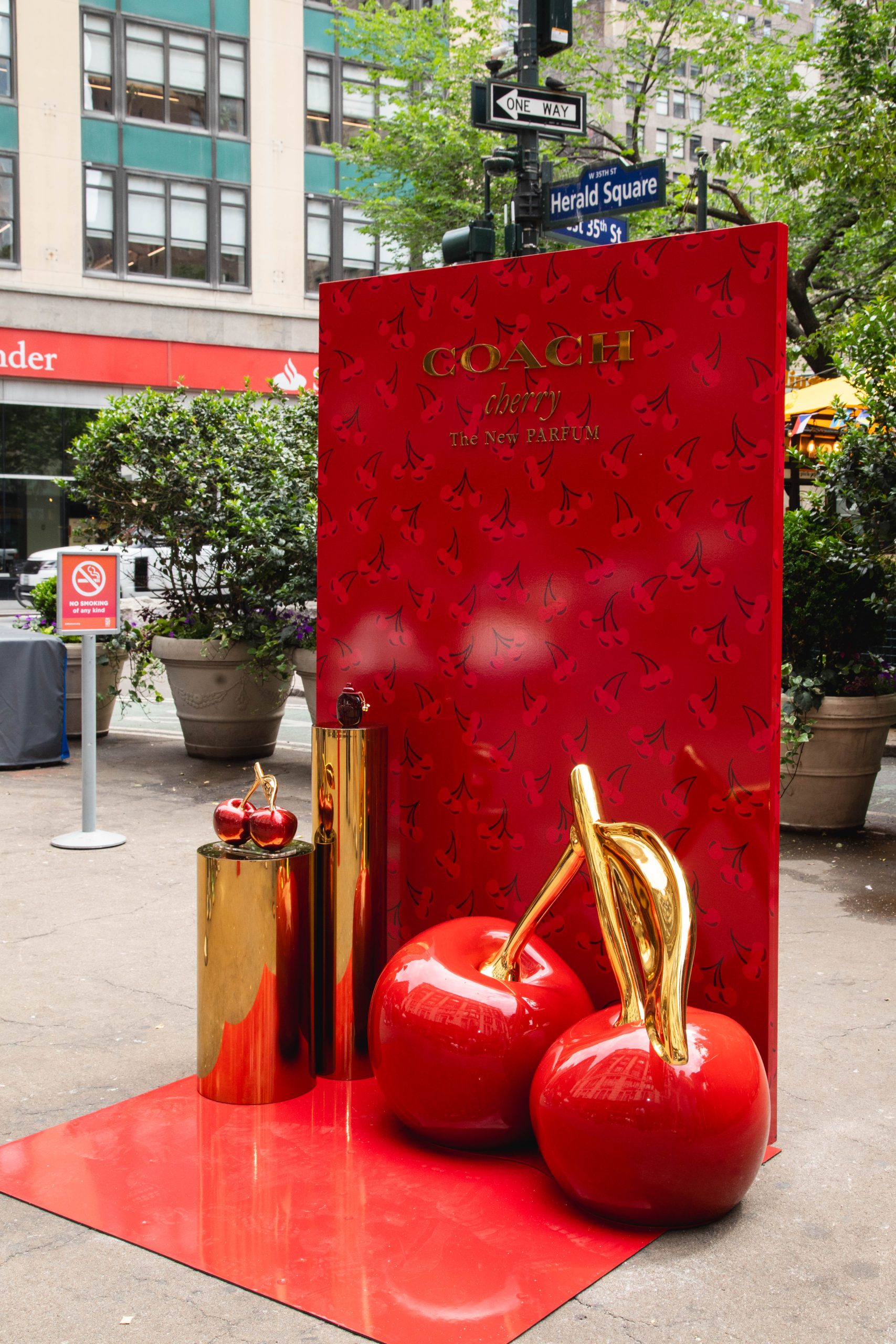 Coach Cherry perfume display with large cherry sculptures and gold stands on a city sidewalk.
