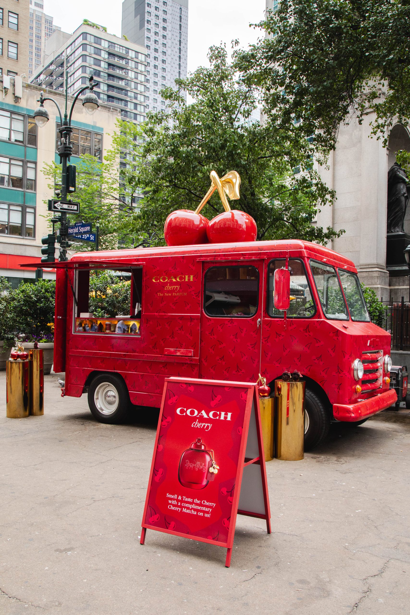 Red food truck with cherry decor and a "COACH Cherry" sign parked near tall buildings and trees.